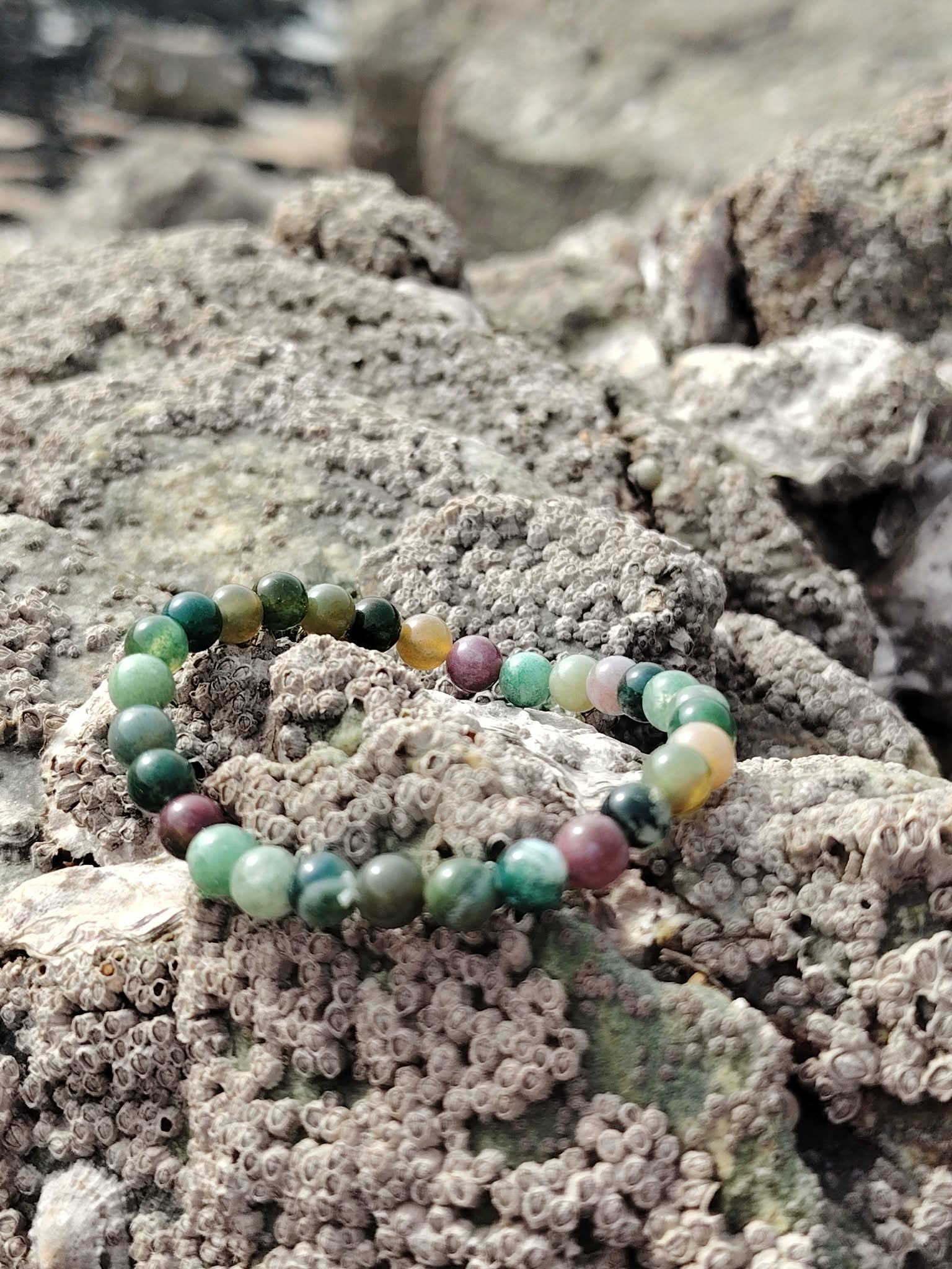 Bracelet agate indienne 6 mm en cercle sur rochers bretons, perles vert d’eau et tons terre au milieu des galets, pour apaiser, ancrer et harmoniser.