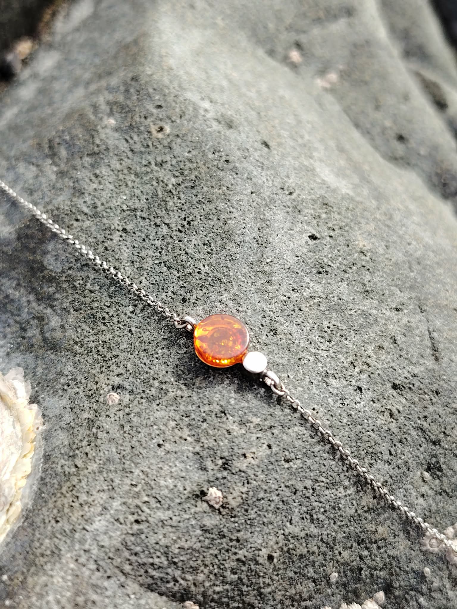Bracelet ambre cognac sur chaîne en argent rhodié posé sur rocher breton, cabochon rond miel, sérénité, cocon rassurant et bien-être apaisé.