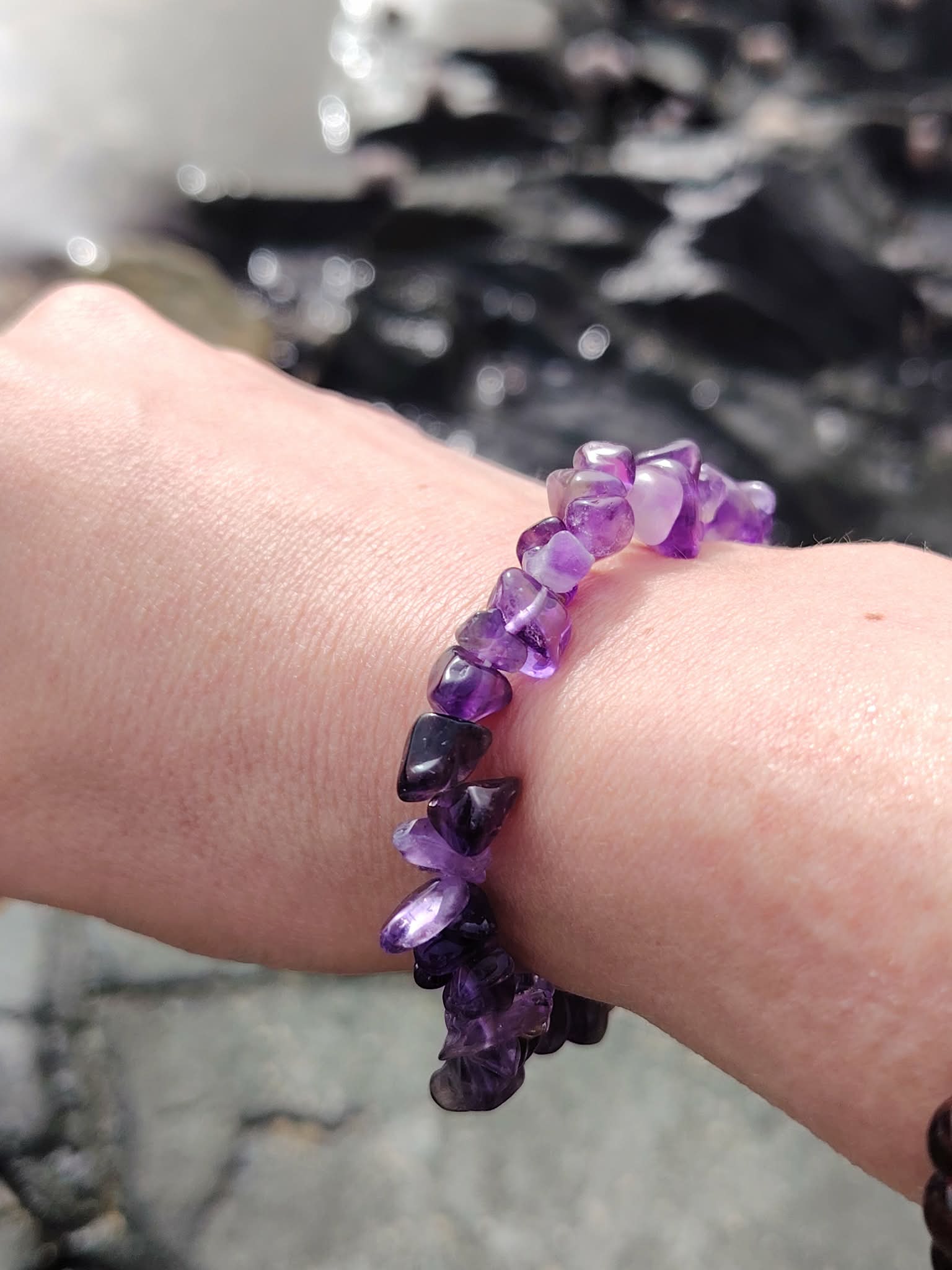 Bracelet améthyste baroque porté au poignet sur rochers en bord de mer, nuances violettes, clarté mentale et énergie apaisante