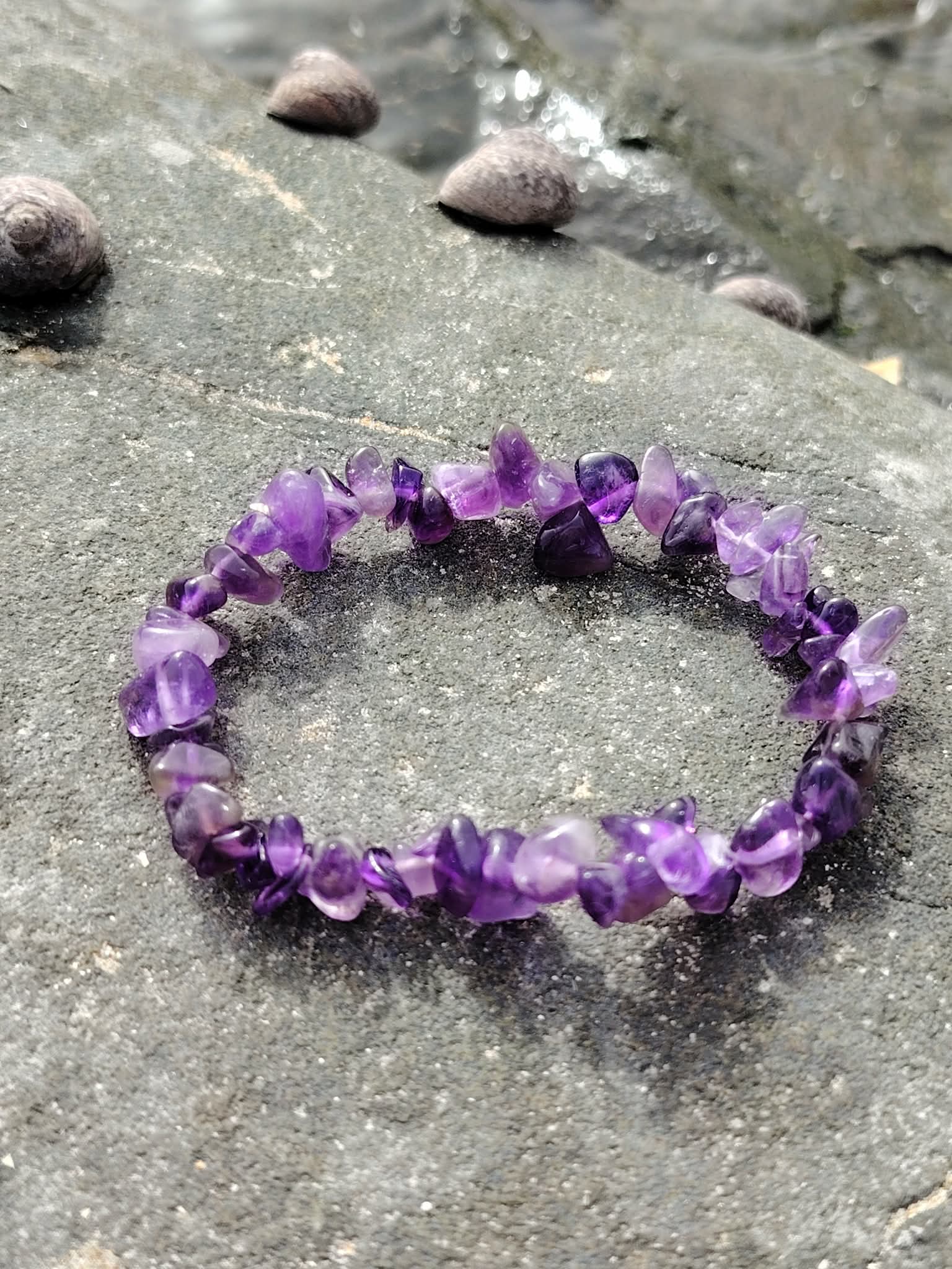 Bracelet baroque en améthyste posé sur sable et galets au bord de l’océan, bijou violet favorisant détente et inspiration