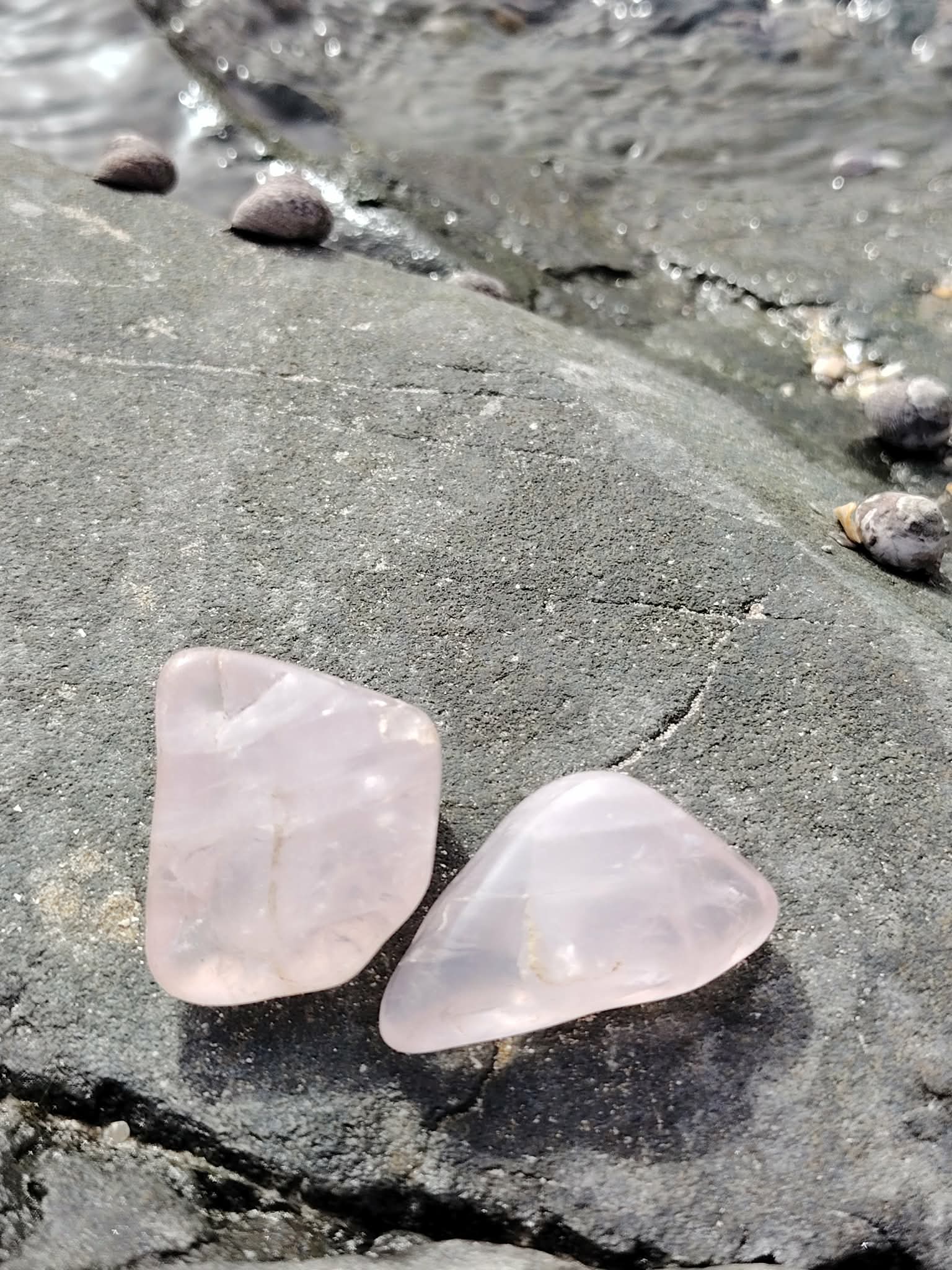 Deux pierres roulées en quartz rose naturel posées sur une roche en Bretagne, pierres naturelles associées à l’amour de soi, à la paix émotionnelle et à la délicatesse intérieure.