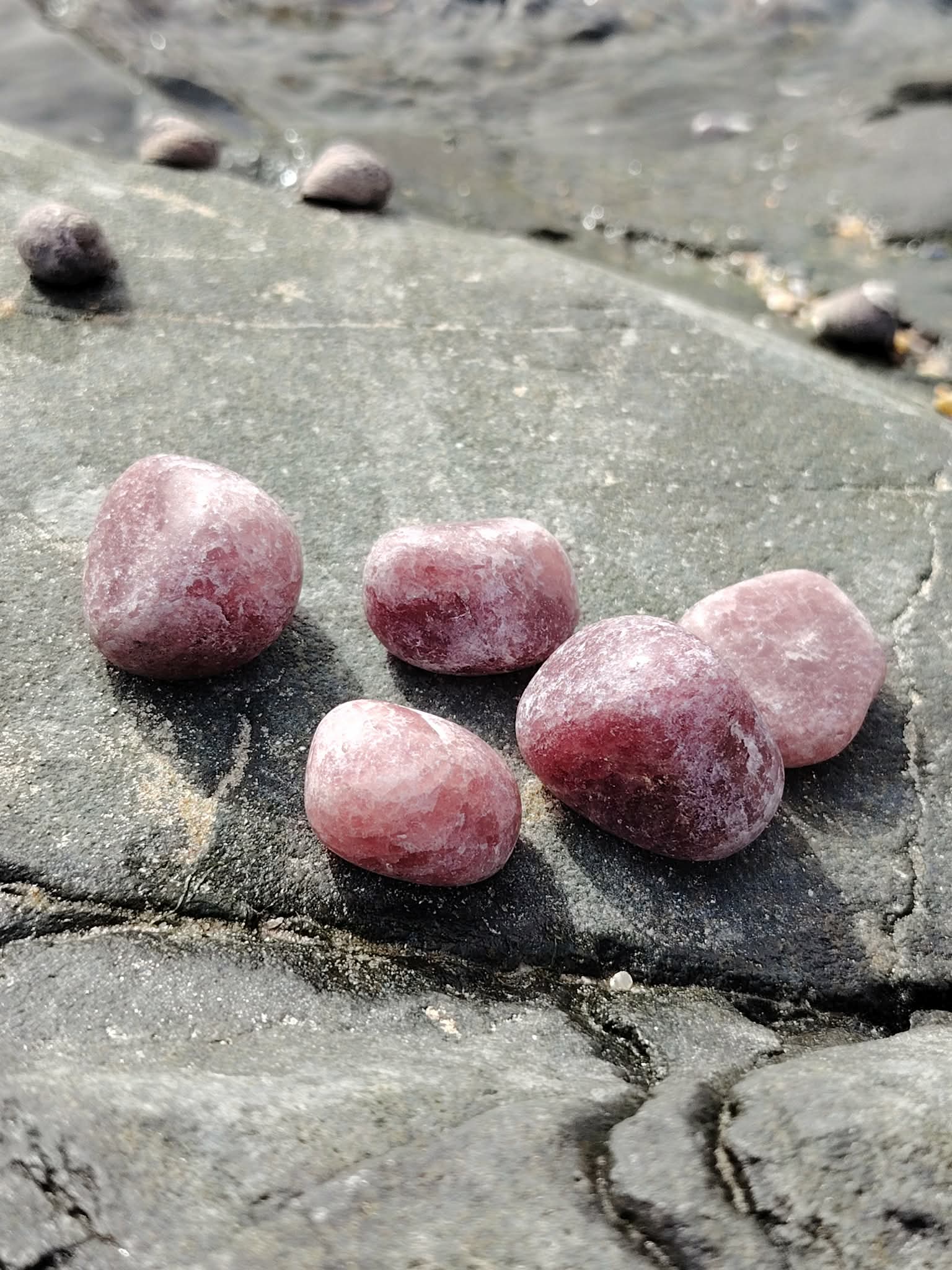 Pierres roulées en quartz fraise naturel posées sur une roche au bord de l’eau en Bretagne, pierres naturelles évoquant la fluidité émotionnelle, la douceur intérieure et la paix du cœur.