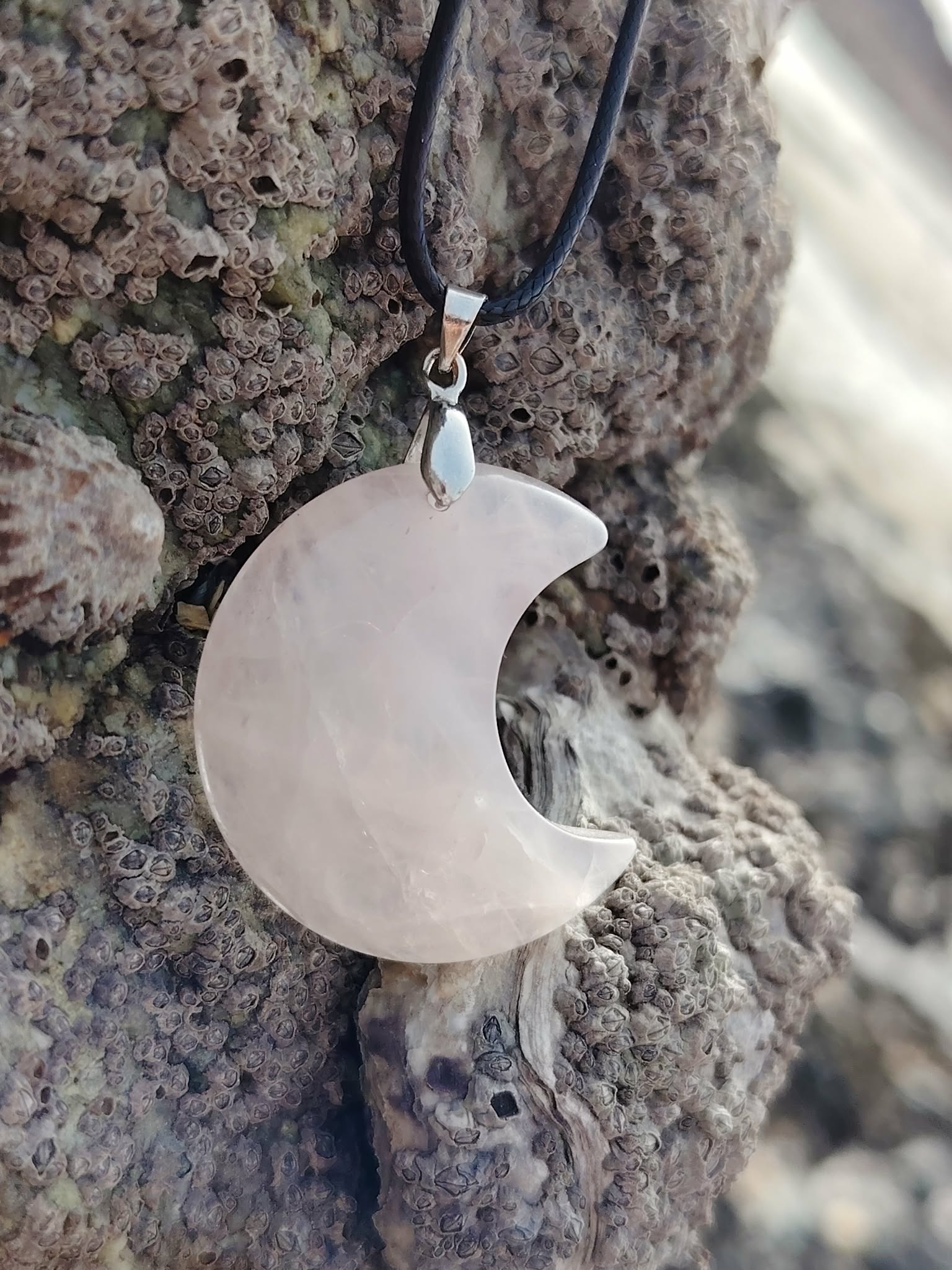 Pendentif lune en quartz rose naturel suspendu sur écorce en décor Bretagne, bijou en pierre naturelle associé à l’apaisement, à la sensibilité et à la paix émotionnelle.