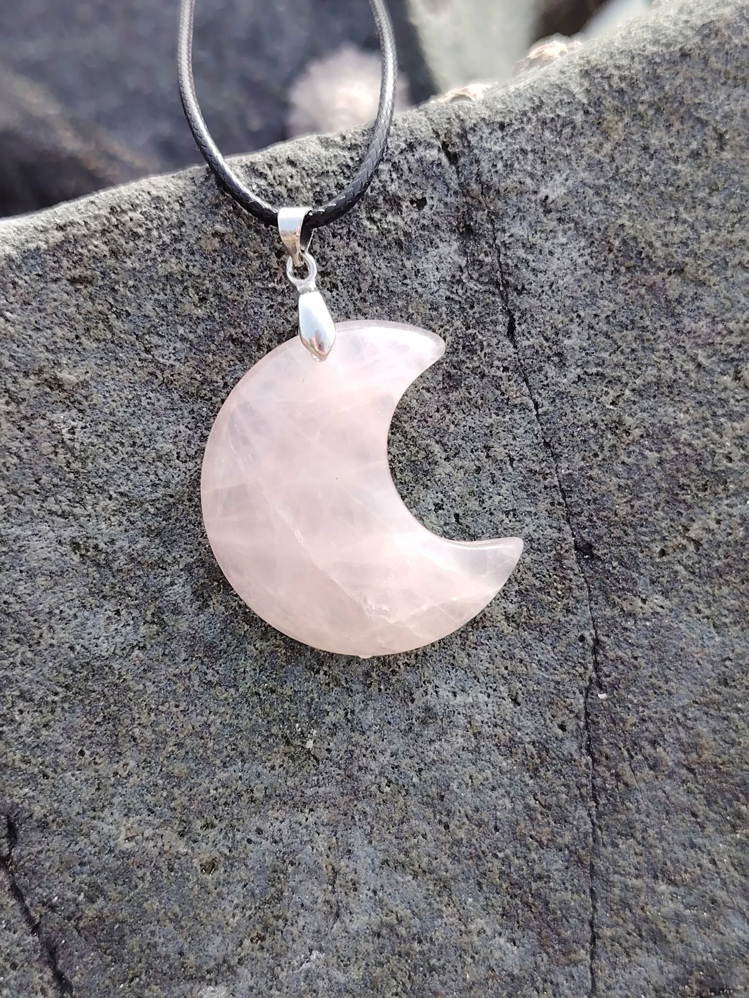 Pendentif lune en quartz rose naturel posé sur roche sombre en Bretagne, bijou en pierre naturelle associé à la tendresse, au réconfort et à la paix du cœur.