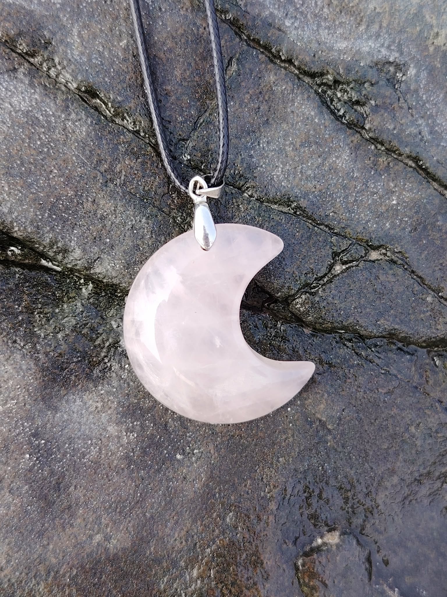 Pendentif lune en quartz rose naturel sur fond de roche sombre, photo Bretagne, collier délicat évoquant la sensibilité, le calme émotionnel et l’harmonie du cœur.