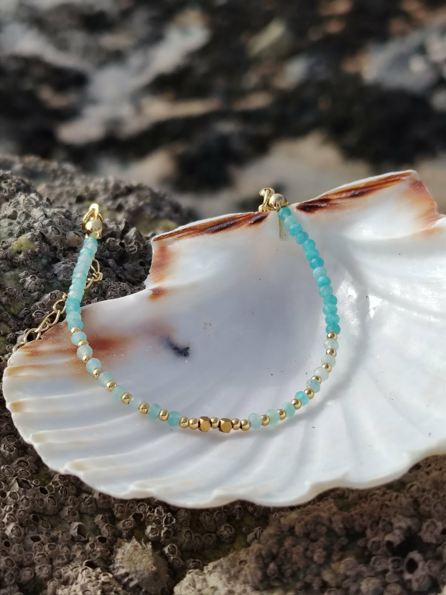 Bracelet amazonite facettée 2 mm et cuivre plaqué or sur coquillage blanc et rocher sombre en Bretagne, bijou fin aux tons bleu-vert pour douceur