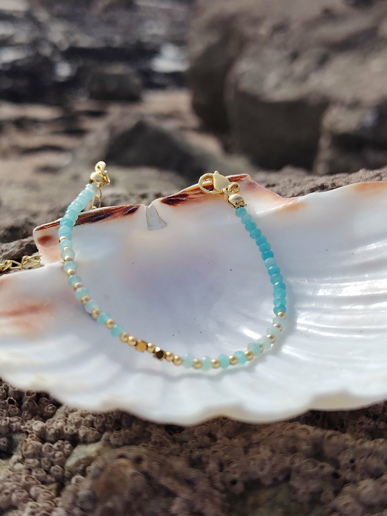 Bracelet amazonite facettée 2 mm sur coquillage blanc en Bretagne, fond rocheux flou et reflets bleu turquoise, élégance et apaisement