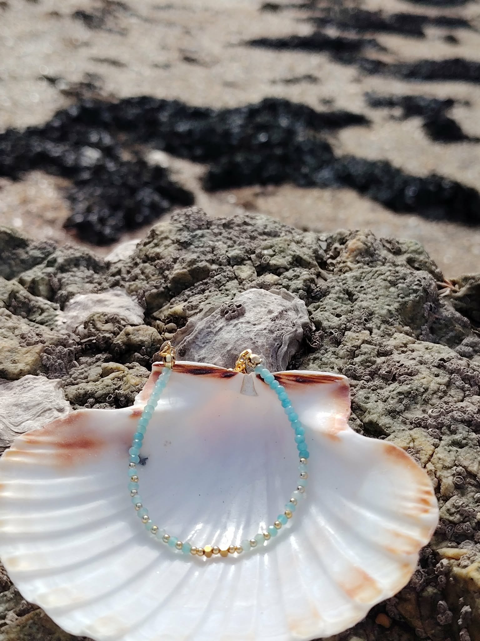 Bracelet fin amazonite naturelle et cuivre plaqué or sur coquillage blanc face à la mer et aux rochers, fluidité émotionnelle