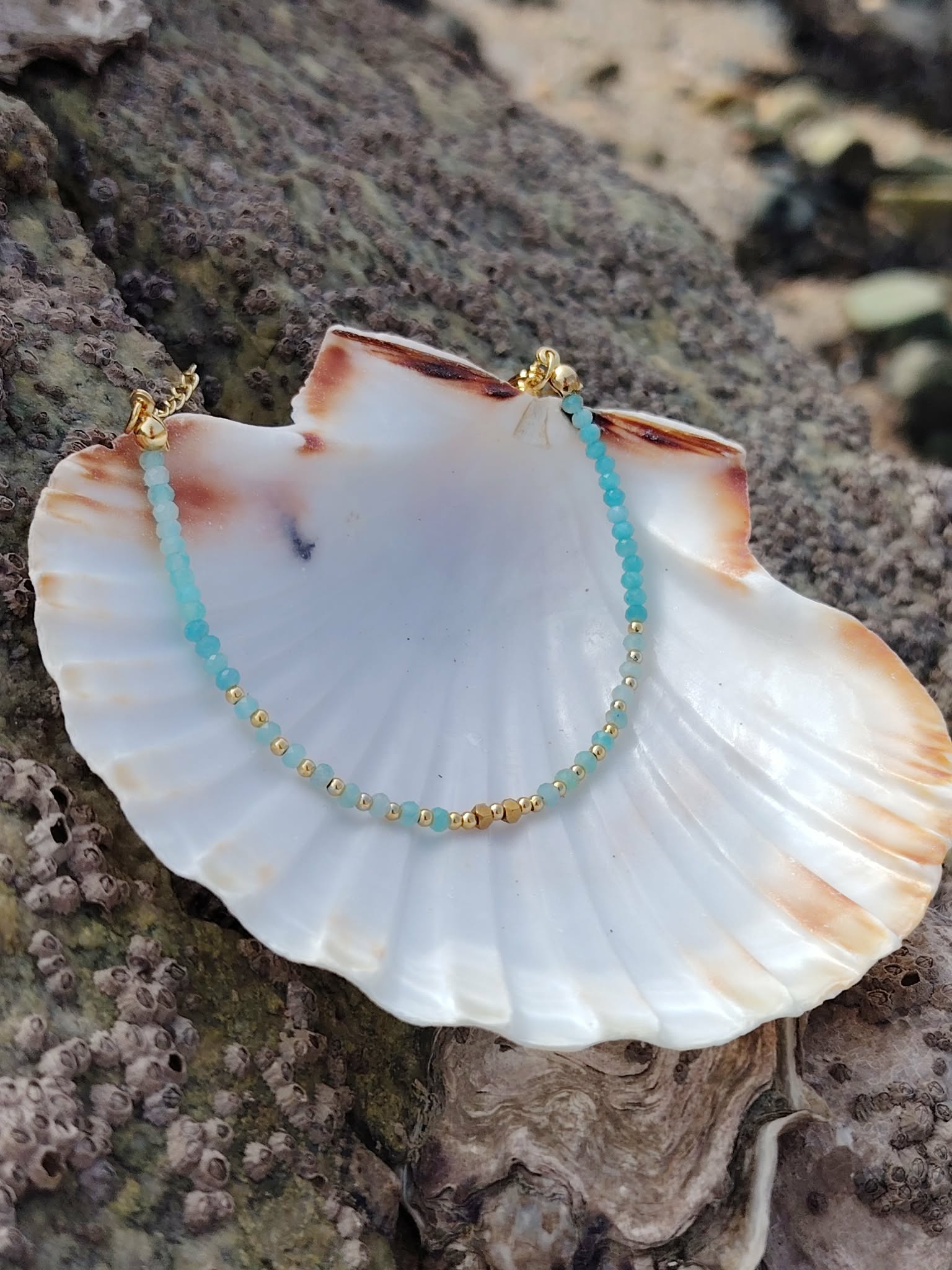 Bracelet fin en amazonite facettée et cuivre plaqué or sur coquillage blanc, photo Bretagne sur roche sombre, harmonie et sérénité