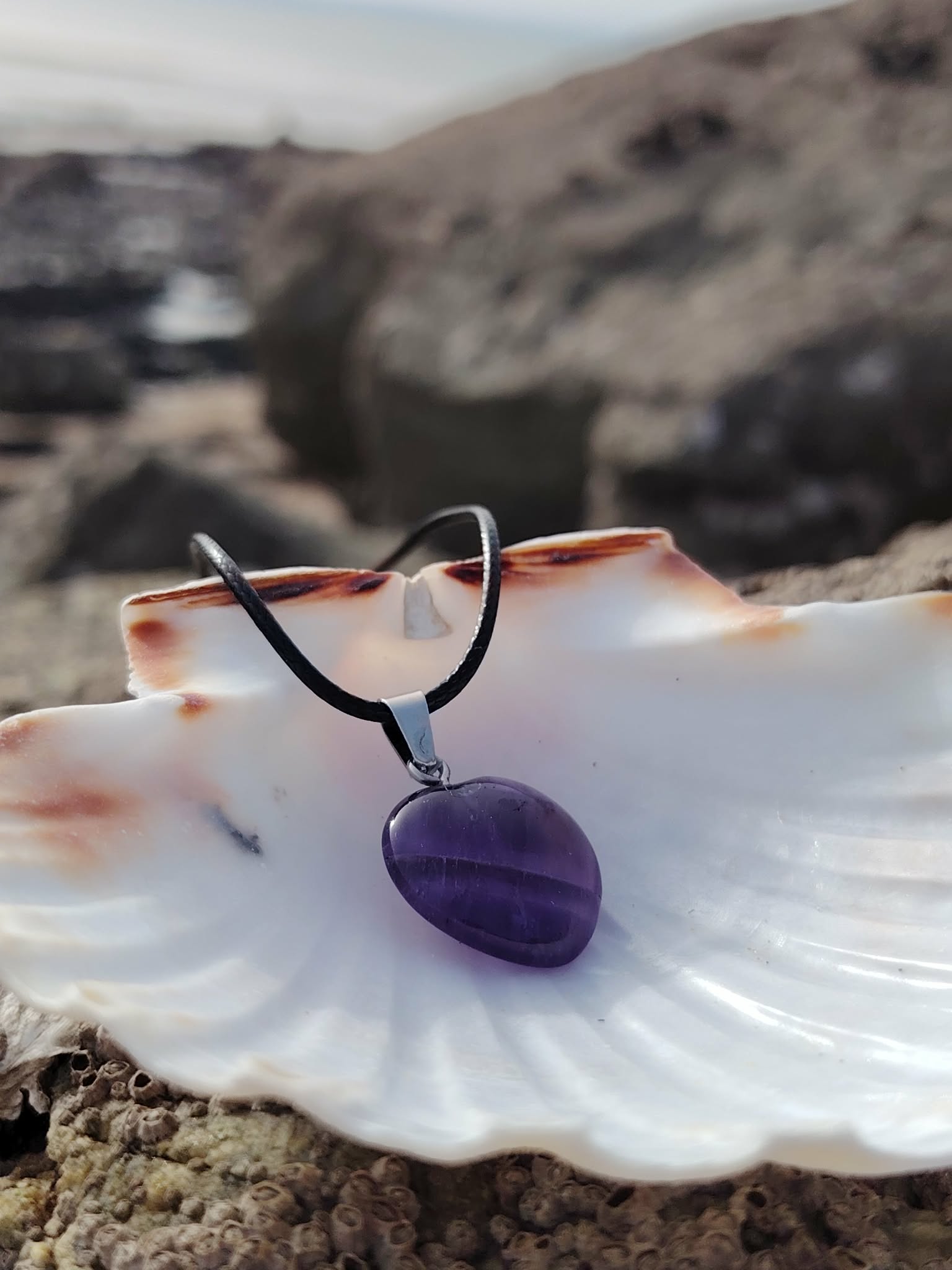 Pendentif améthyste sur cordon noir présenté sur un coquillage face à la mer, sérénité mentale et écoute intérieure