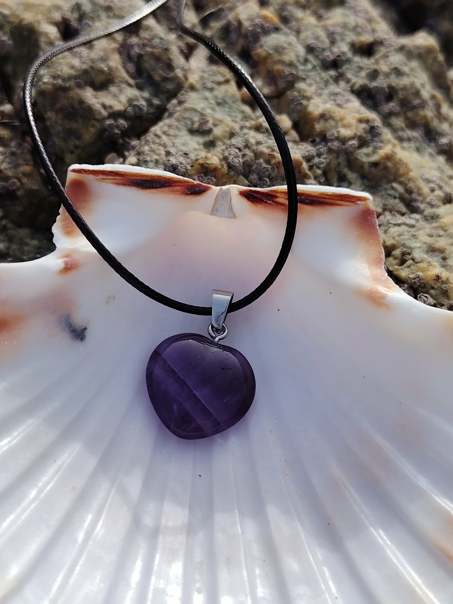 Pendentif cœur en améthyste sur cordon noir, posé sur un coquillage parmi les rochers en Bretagne, harmonie du ressenti et présence plus douce