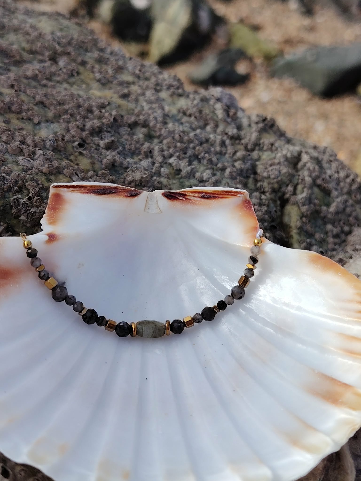 Bracelet labradorite sur chaîne dorée dans un coquillage nacré face aux rochers, écoute subtile et harmonie intérieure
