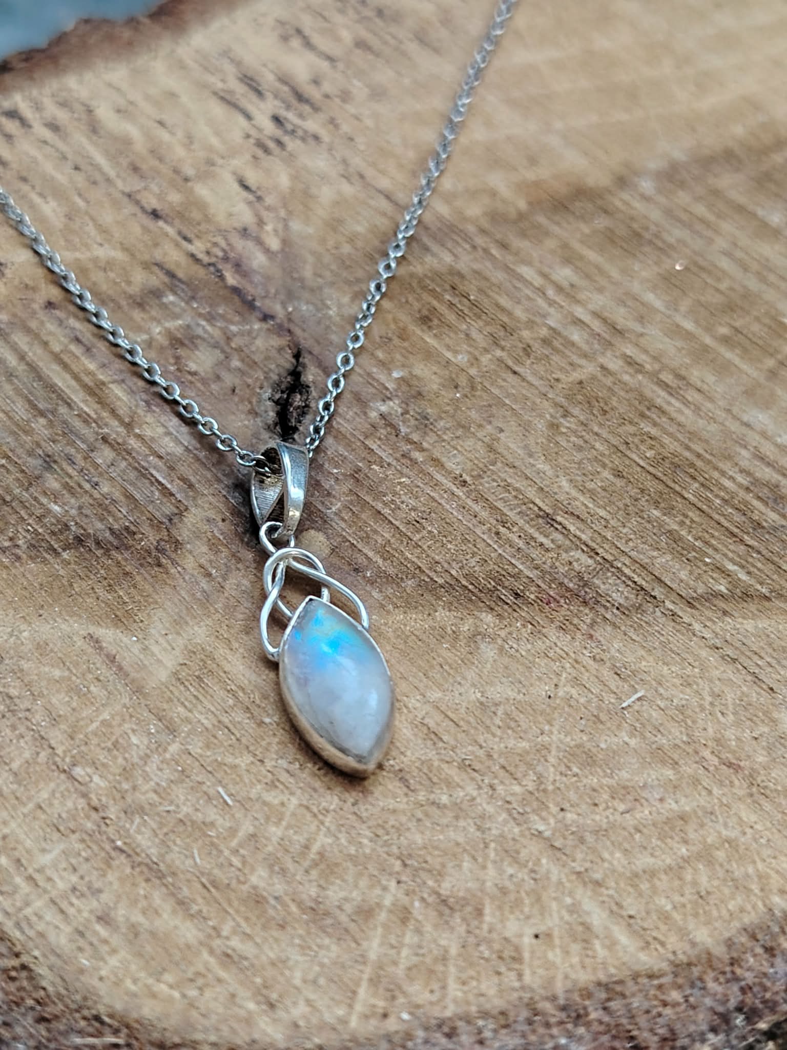 Pendentif elfique en péristérite argent 925 avec chaîne en acier inoxydable, posé sur bois naturel aux veines marquées, reflet bleu irisé, décor chaleureux évoquant intuition, calme et douceur.