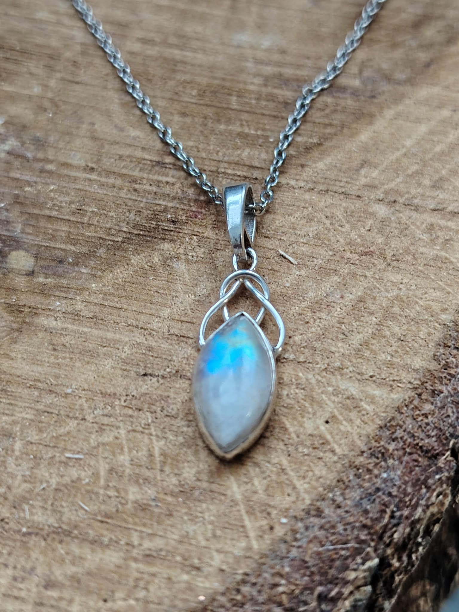 Pendentif elfique en péristérite argent 925 avec chaîne en acier inoxydable, présenté sur bois naturel aux teintes chaudes, reflet bleu lumineux, décor sobre évoquant intuition, sérénité et douceur.