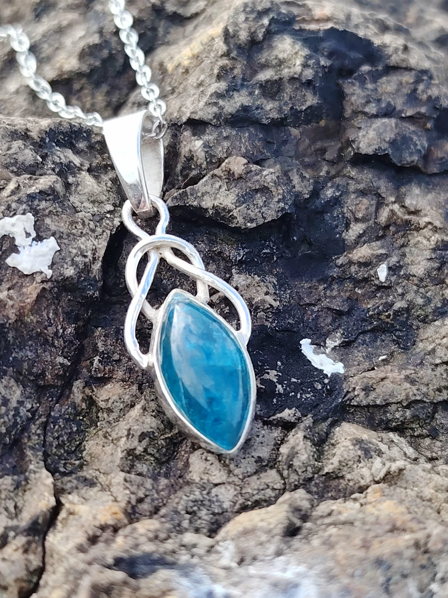 Pendentif elfique en apatite bleue et argent 925 posé sur un rocher breton aux teintes minérales, bijou en pierre naturelle associé à l’inspiration, à la parole fluide et au calme intérieur.