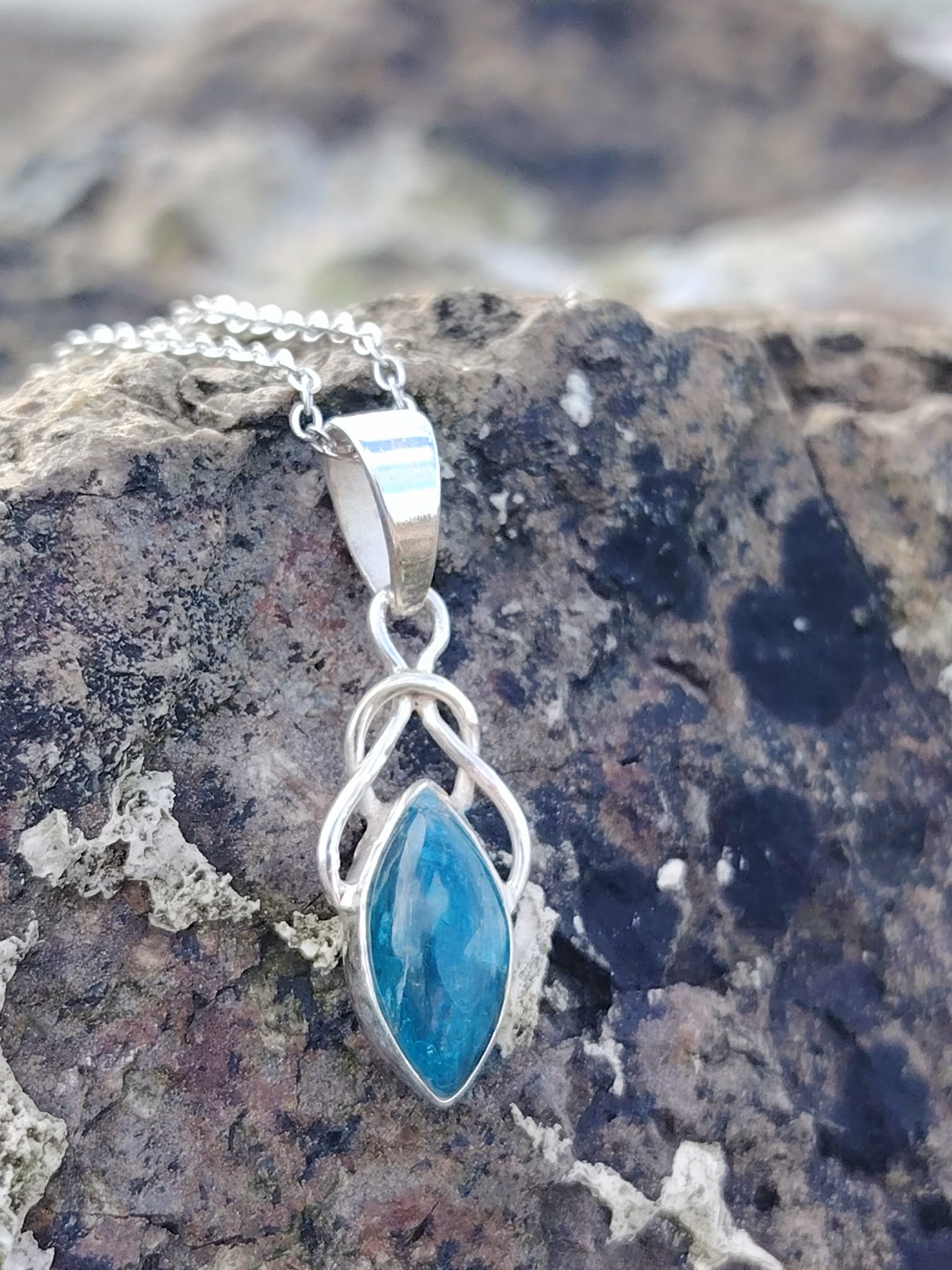 Pendentif elfique en apatite bleue et argent 925 posé sur un rocher breton dans une ambiance naturelle et minérale, bijou en pierre naturelle relié à l’inspiration, au discernement et à la tranquillité intérieure.
