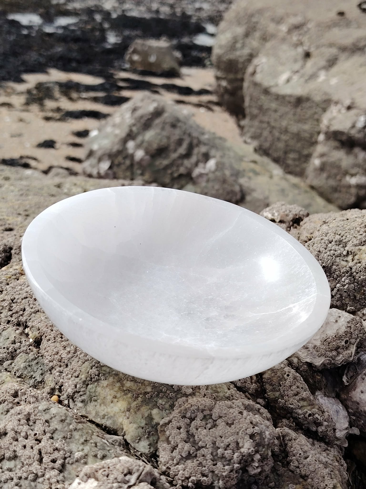 Bol en sélénite 15 cm photographié sur les rochers en Bretagne, dans un décor minéral naturel, inspirant purification, sérénité et clarté émotionnelle au quotidien.