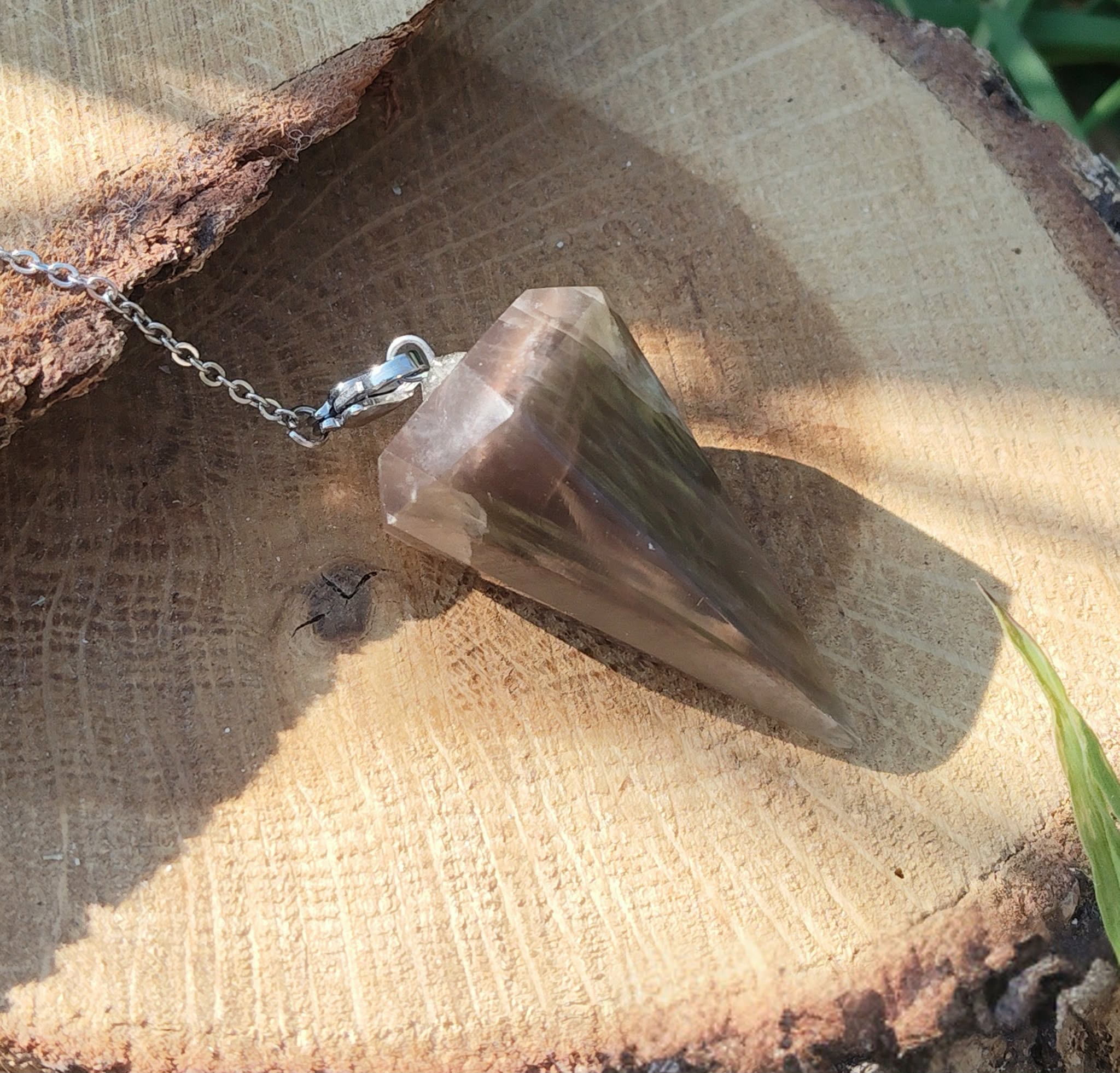 Pendule en pierre de lune noire posé sur une tranche de bois, éclairé par une lumière chaude, dans une ambiance naturelle et apaisante évoquant intuition, ancrage et protection intérieure.