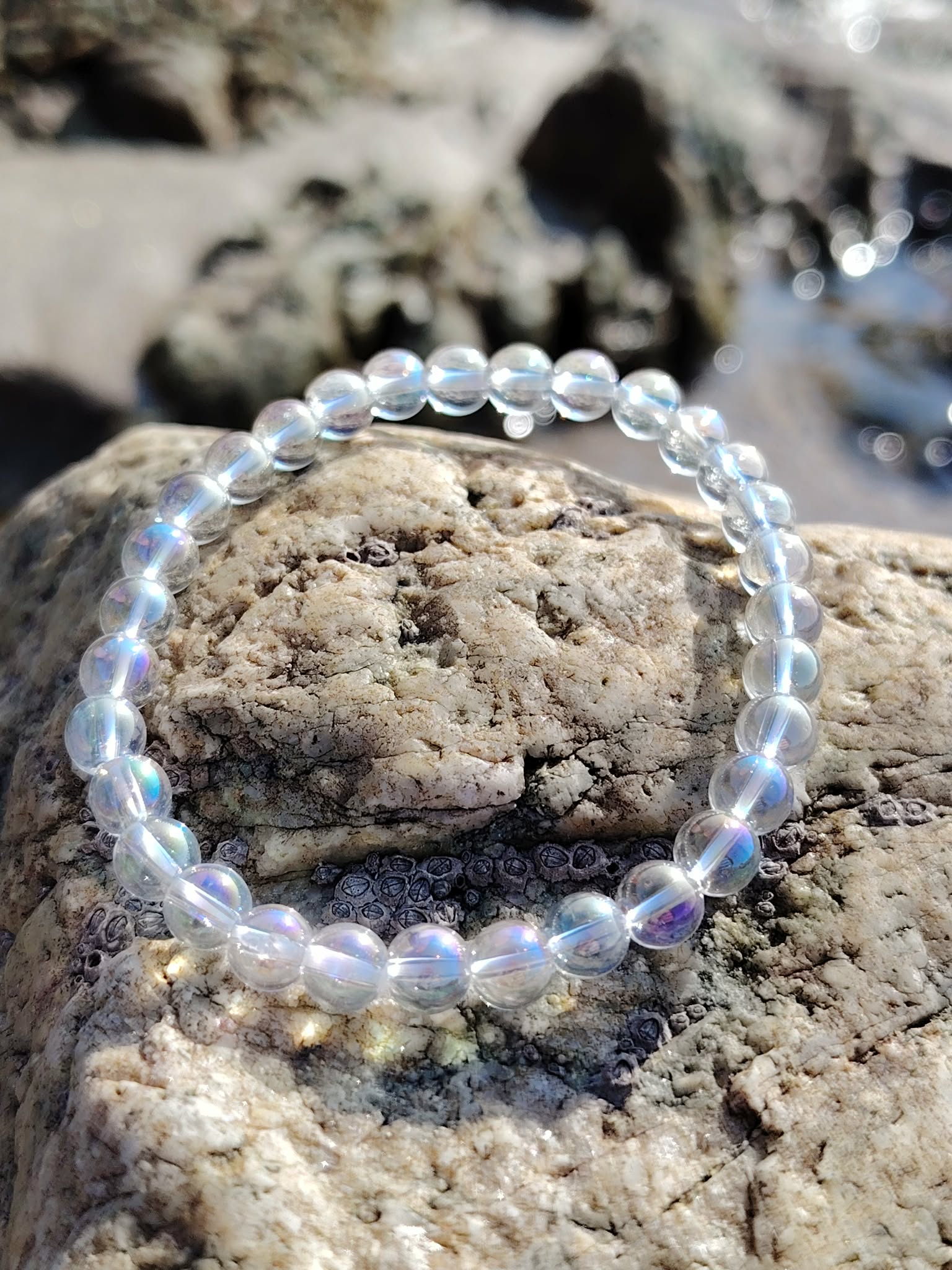 Bracelet Angel Aura aux perles irisées sur rochers en ambiance marine lumineuse, création apaisante en cristal de roche 6 mm.
