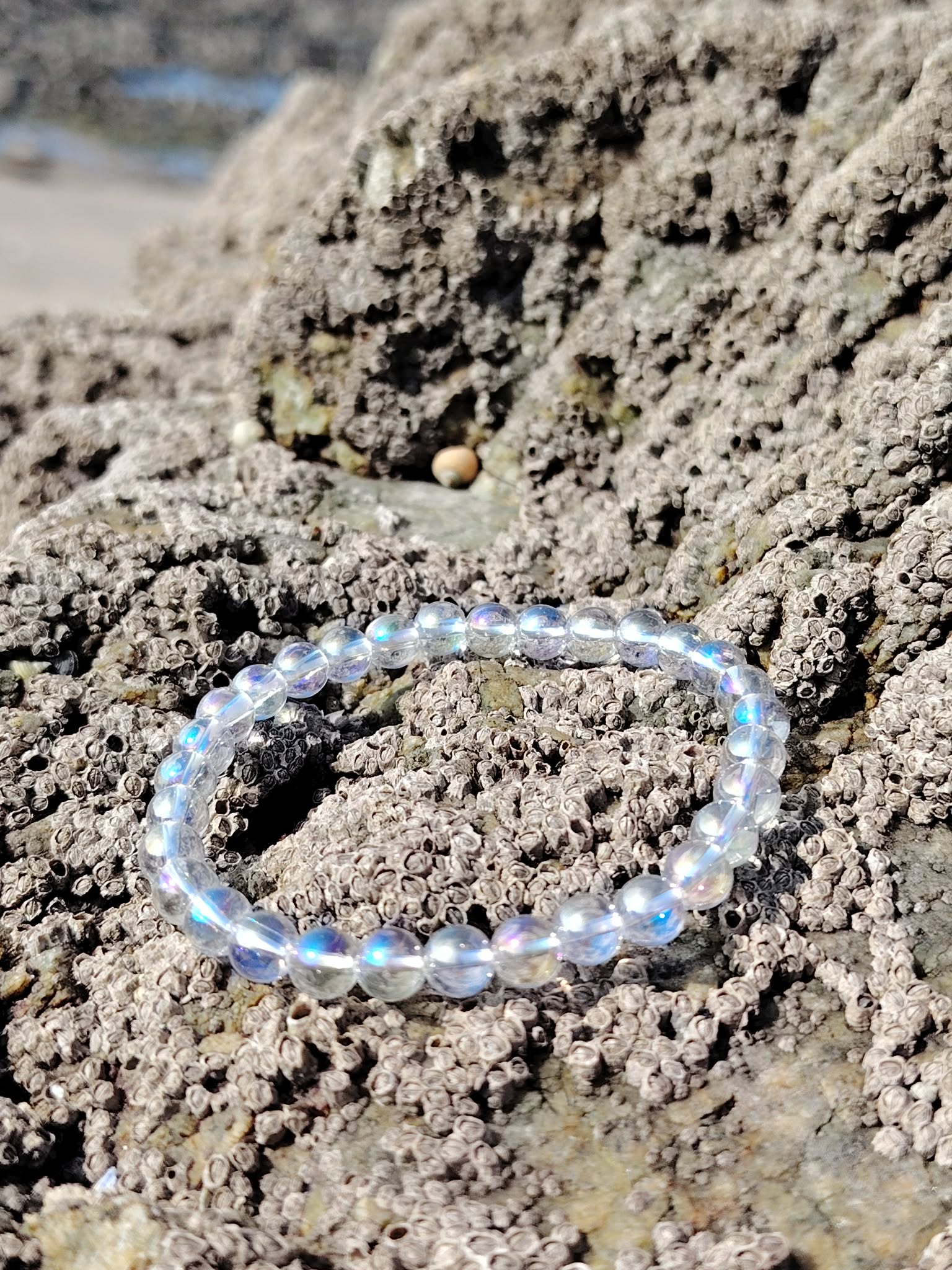Bracelet Angel Aura Quartz sur rochers minéraux en Bretagne, reflets irisés bleutés, bracelet 6 mm pour douceur et recentrage