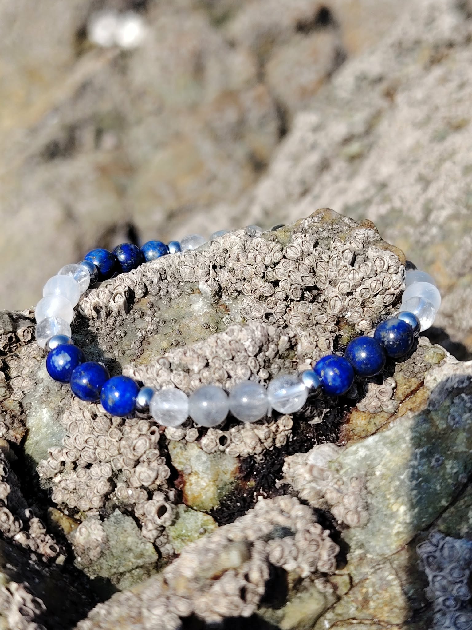 Bracelet migraine en lapis-lazuli, labradorite et sélénite 6 mm, posé entre les rochers bretons dans une ambiance naturelle de douceur, d’apaisement et d’harmonie intérieure.