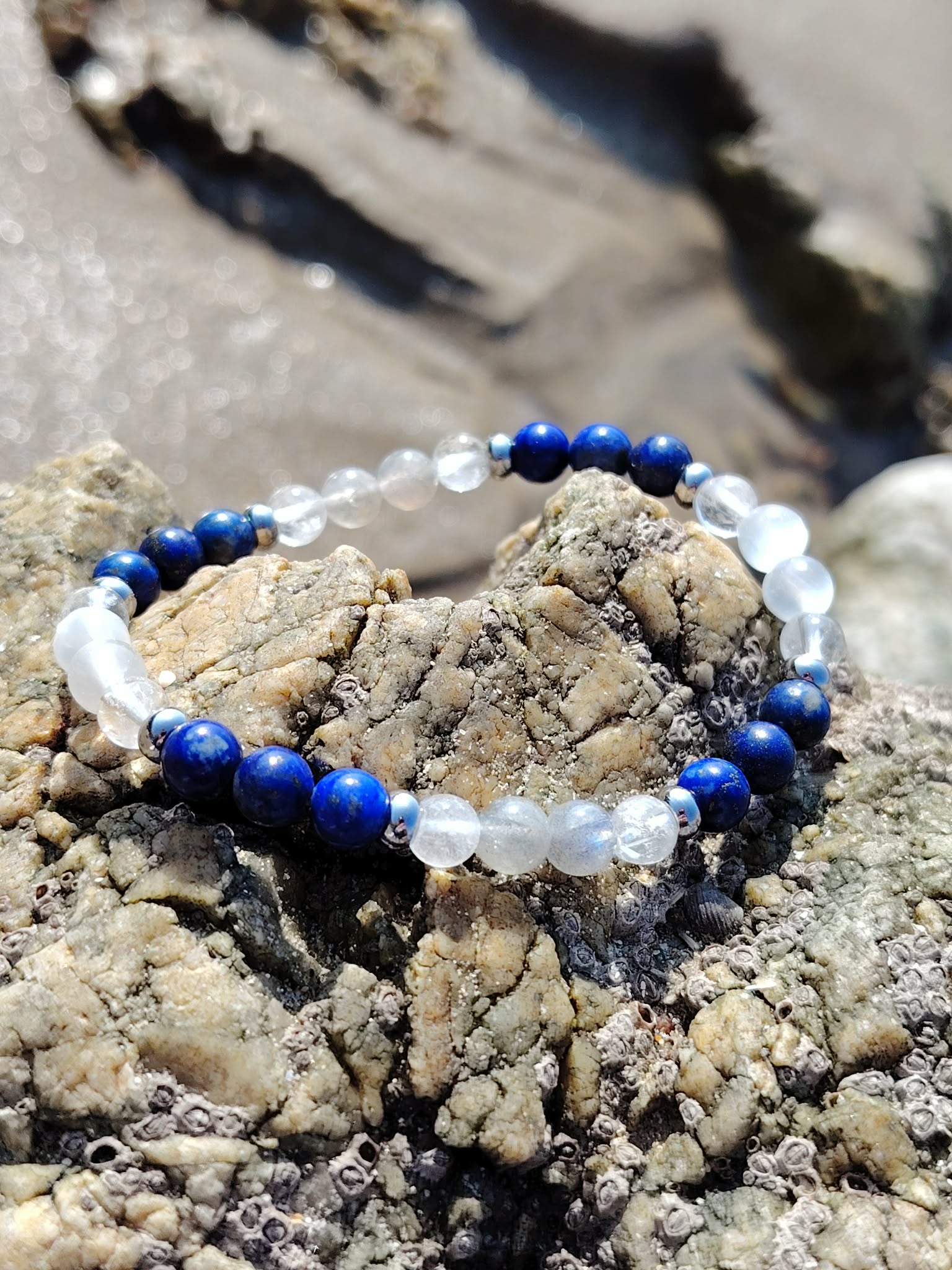 Bracelet migraine en lapis-lazuli, labradorite et sélénite 6 mm, posé sur les rochers de Bretagne près de l’eau, dans une ambiance naturelle de calme, d’harmonie et de clarté