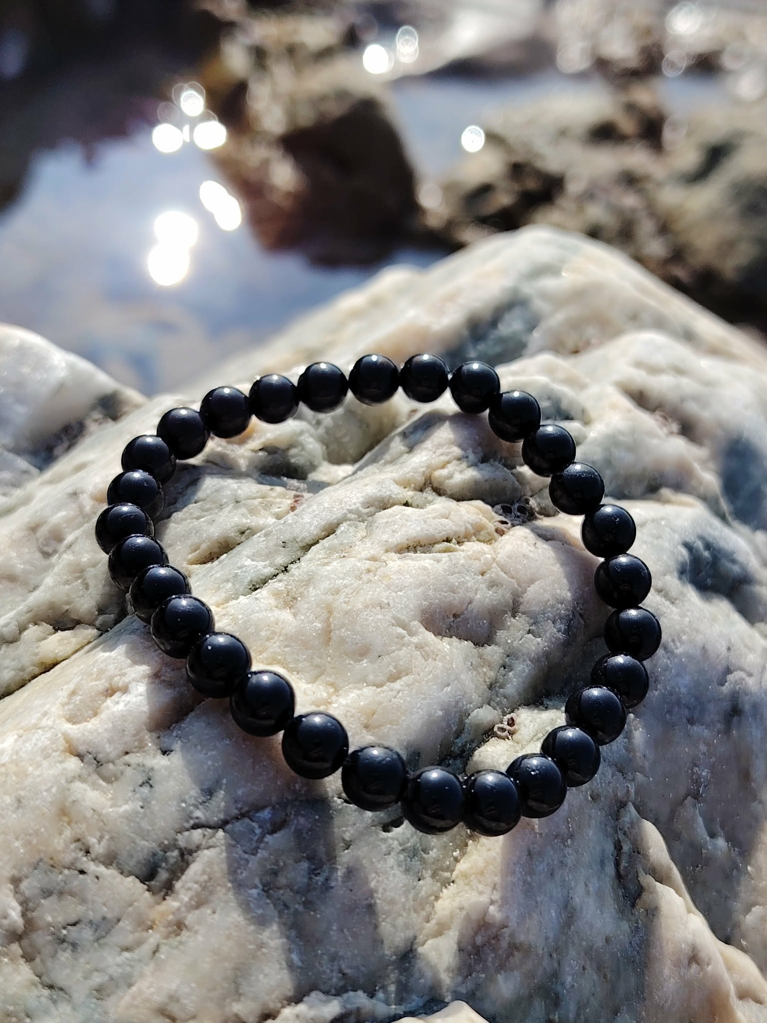 Bracelet tourmaline noire 6 mm posé sur galet brut gris, ambiance nature en Bretagne, calme du mental, enracinement et tenue émotionnelle