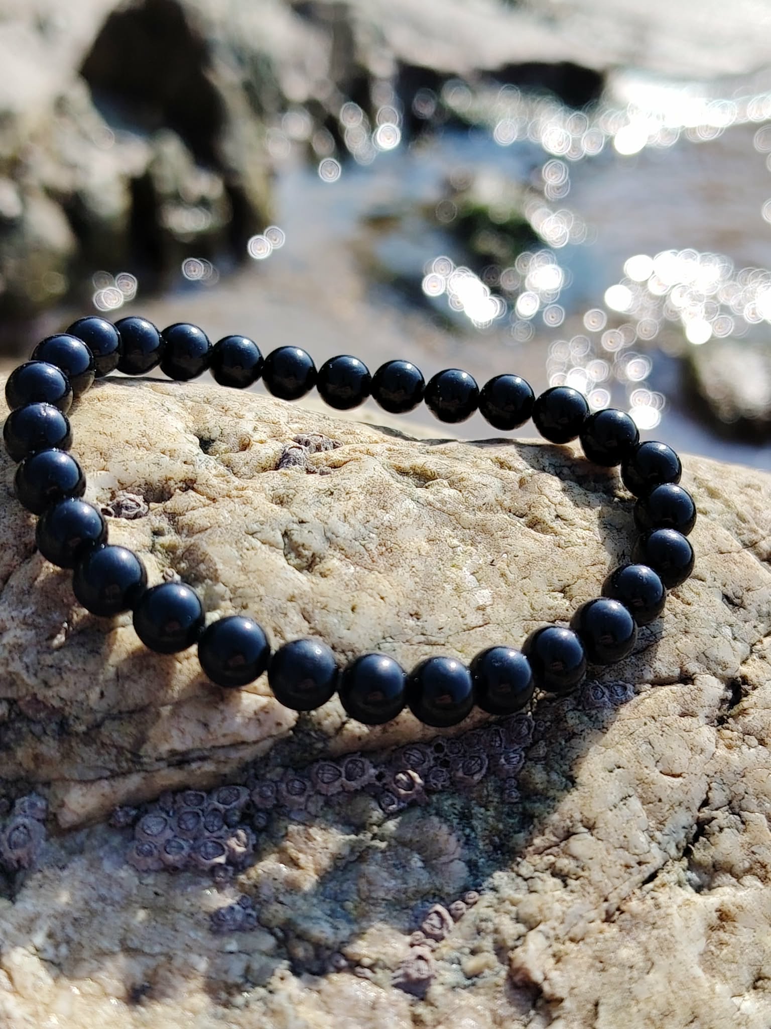 Bracelet tourmaline noire 6 mm sur roche claire veinée en décor minéral breton, bouclier énergétique, ancrage profond et force tranquille