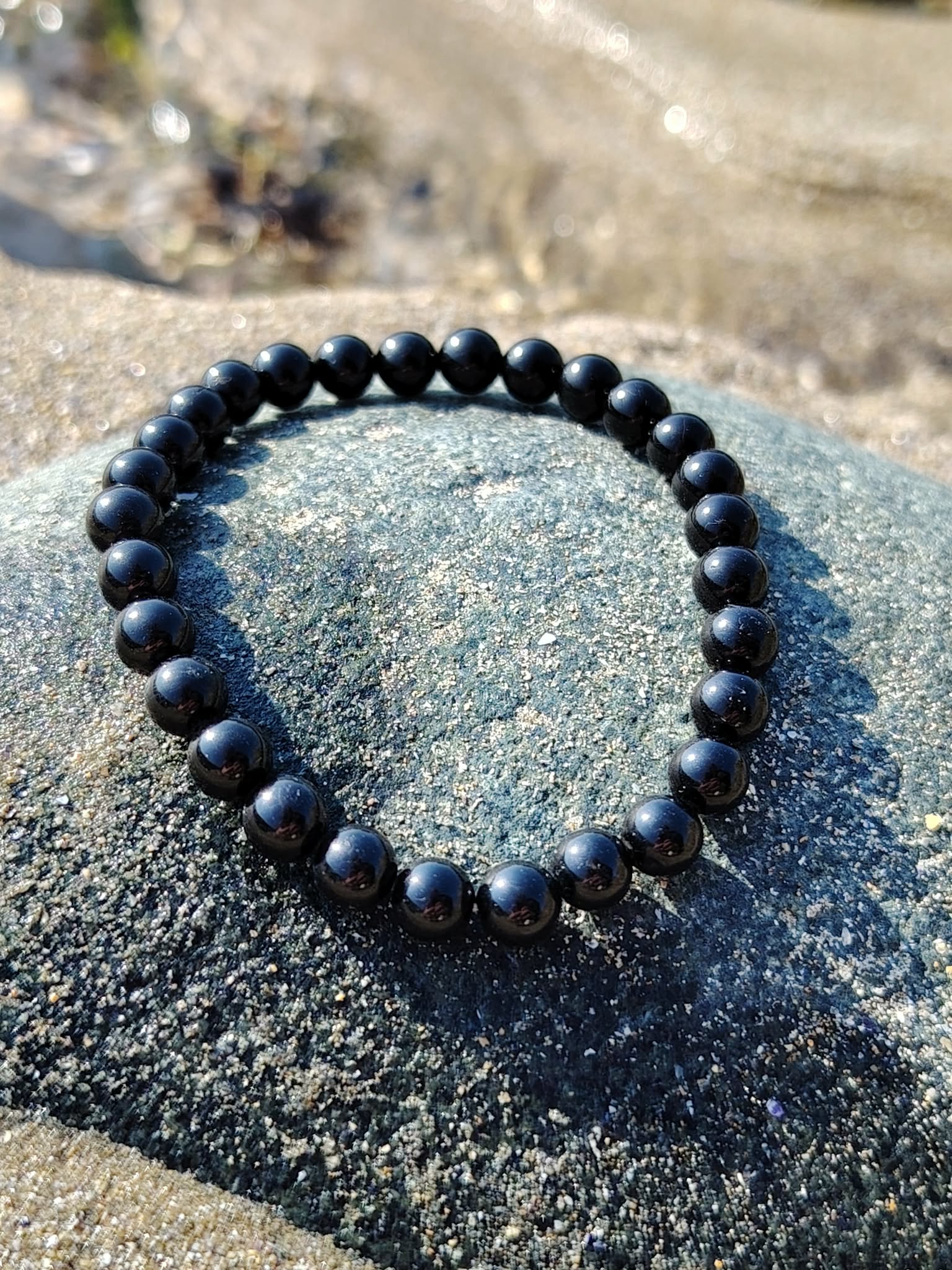 Bracelet tourmaline noire 6 mm posé en cercle sur galet gris brut, lumière naturelle, protection stable et solidité face aux tensions extérieures