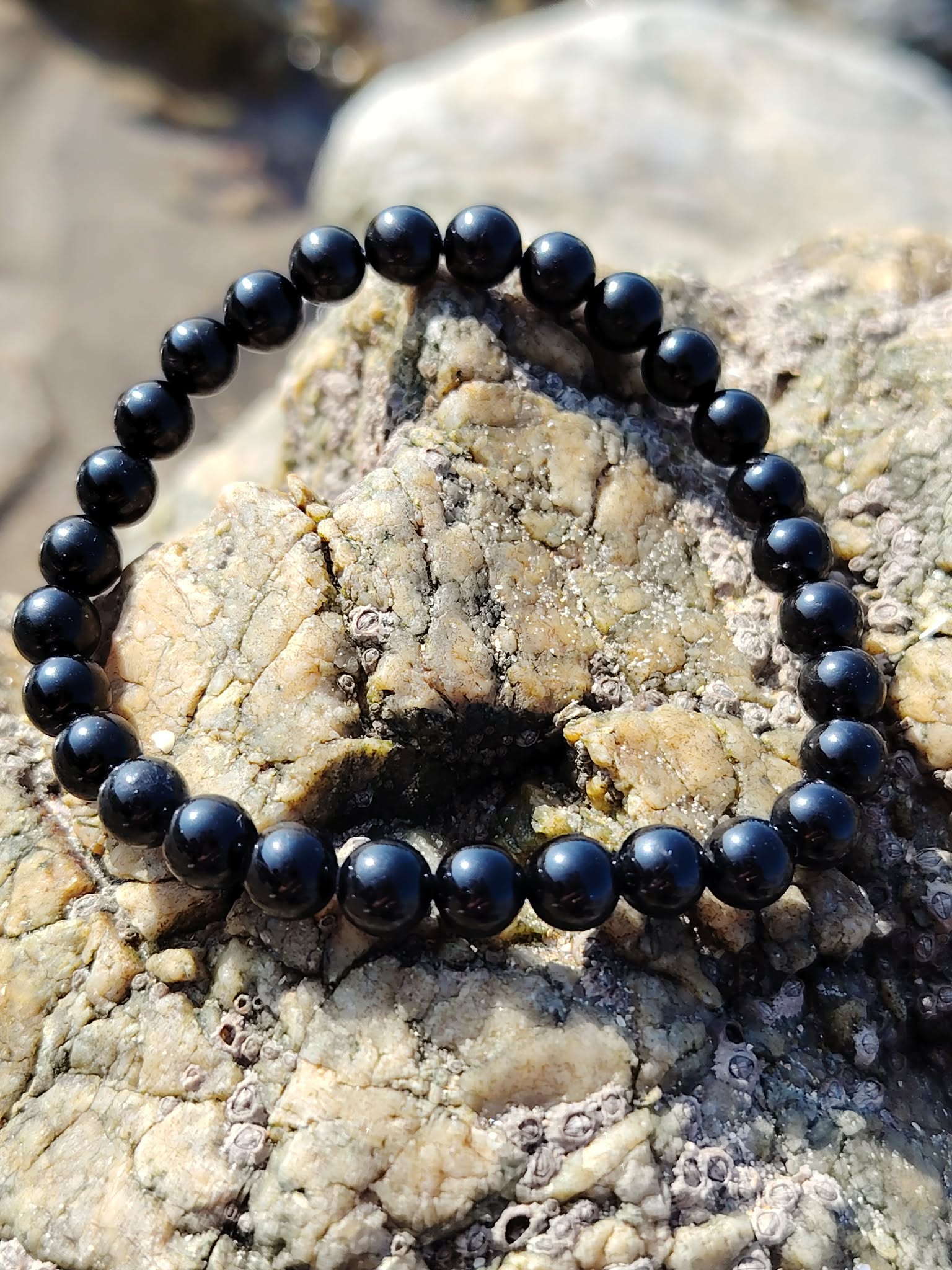 Bracelet tourmaline noire 6 mm en perles rondes sur pierre brute claire, ambiance minérale douce, courage calme et ancrage protecteur