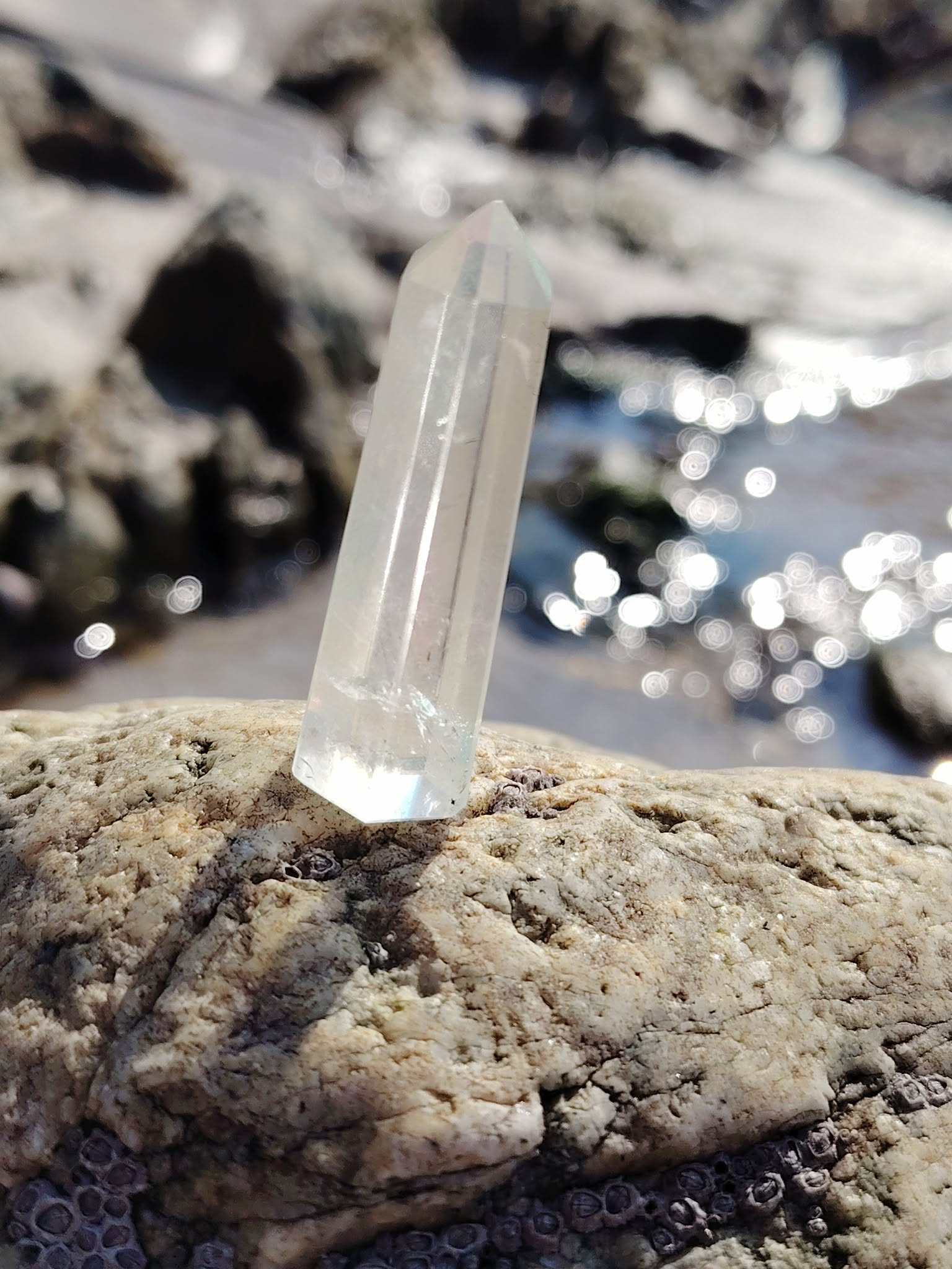 Pointe Angel Aura dressée sur les rochers en Bretagne, baignée de lumière près de l’eau, pierre aux reflets irisés associée à la douceur, à la paix intérieure et à l’élévation.