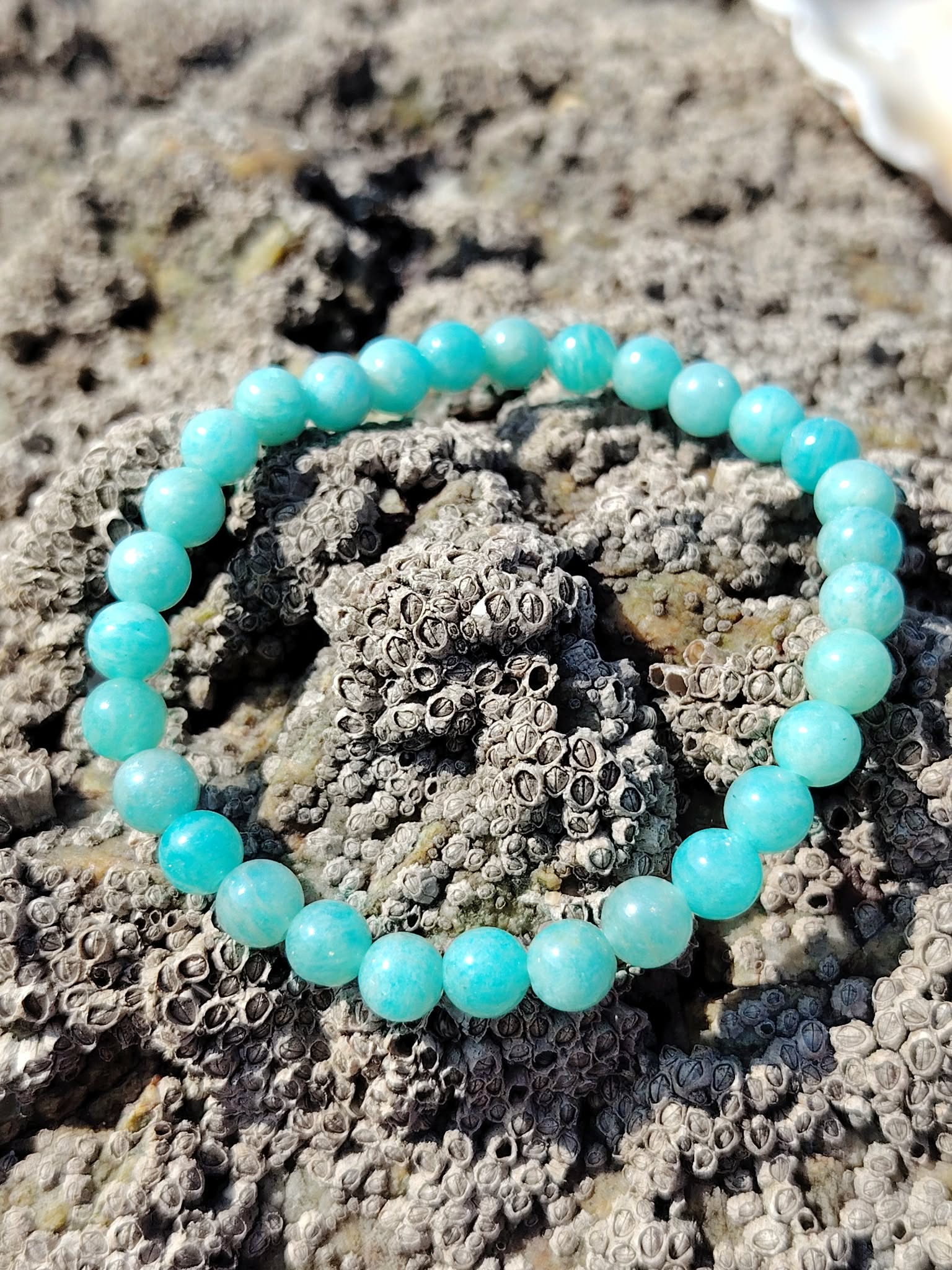 Bracelet en amazonite naturelle 6 mm sur roche granitique en bord de mer, nuances bleu-vert, pierre de réconfort et d’apaisement du mental