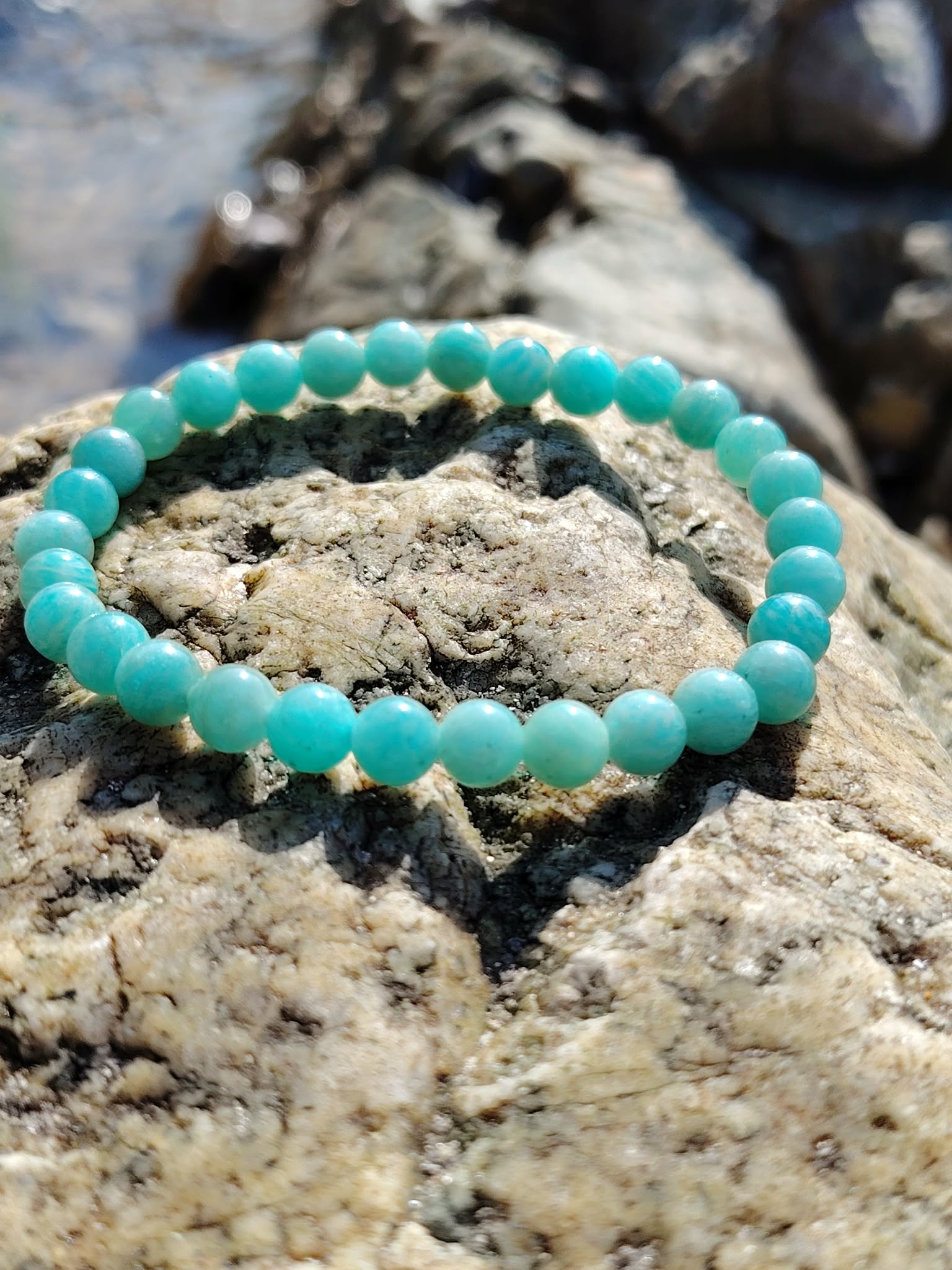 Bracelet amazonite 6 mm sur rocher brut dans un décor minéral, perles bleu lagon liées à la détente, à l’équilibre émotionnel et à la parole apaisée.