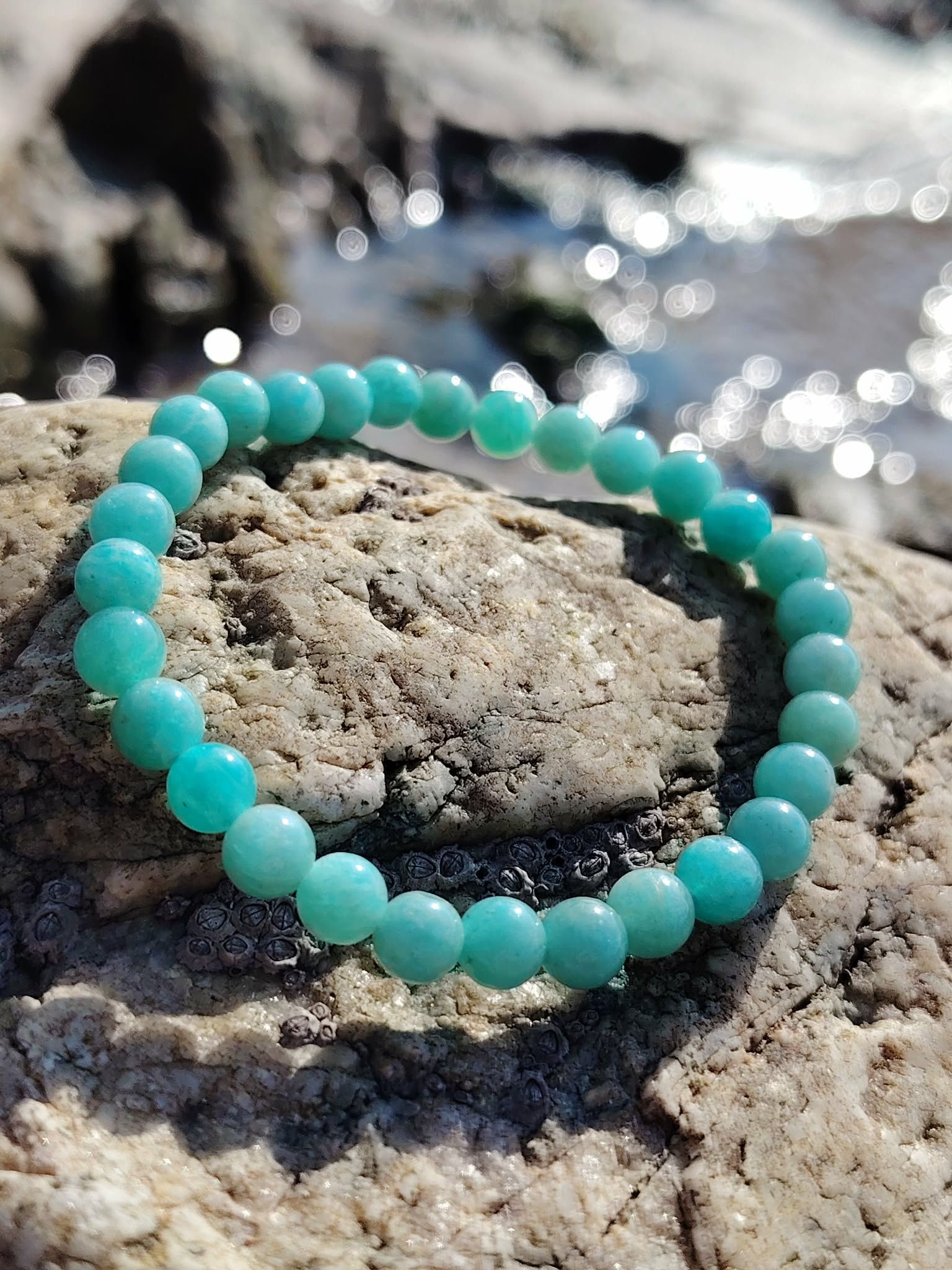 Bracelet amazonite 6 mm sur rochers bretons au bord de l’eau, perles bleu-vert en pierre naturelle, apaisement émotionnel et communication fluide