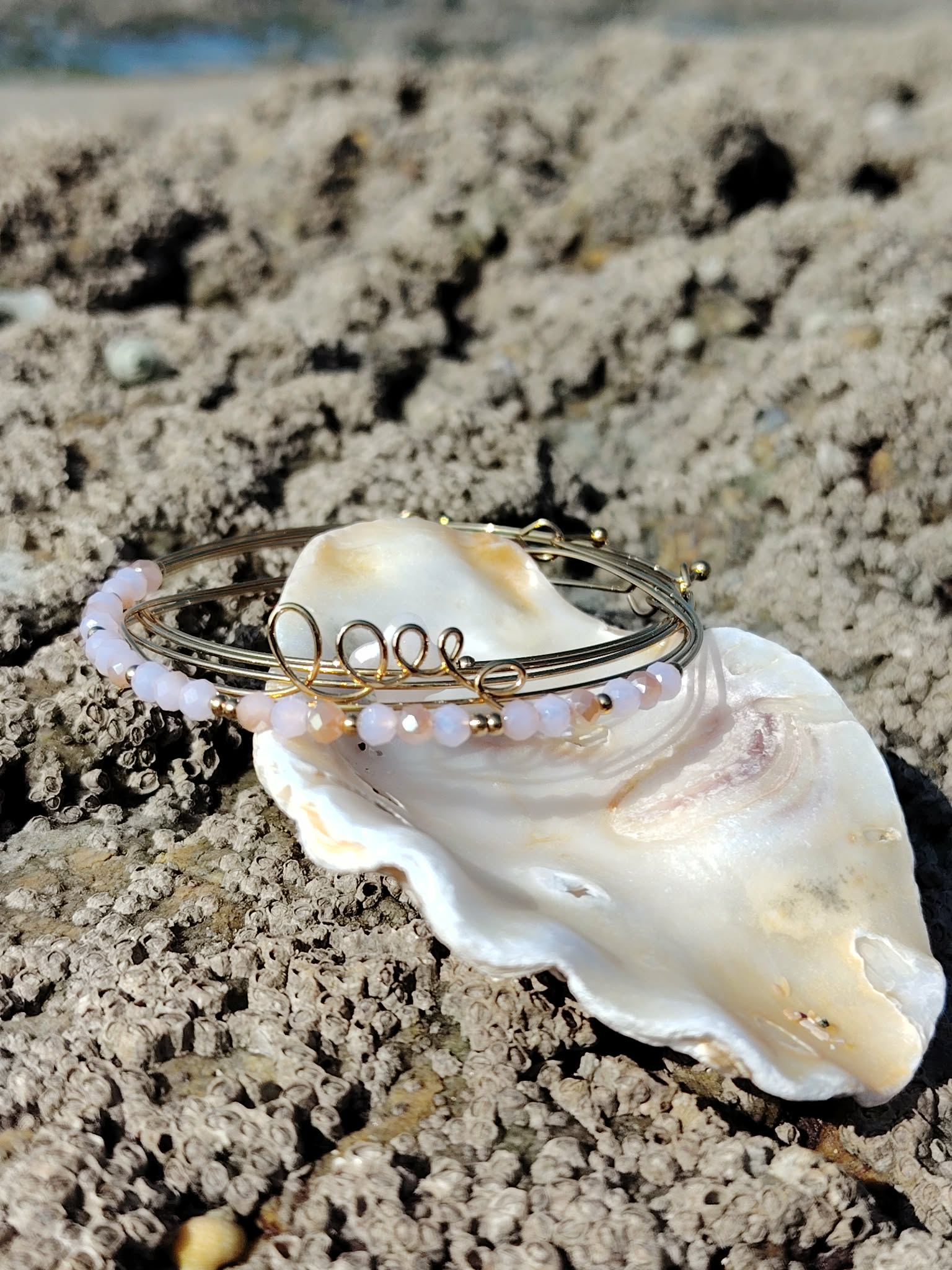 Bracelet semainier Love quartz rose dans un coquillage sur rochers en Bretagne, inspiration marine et amour de soi.