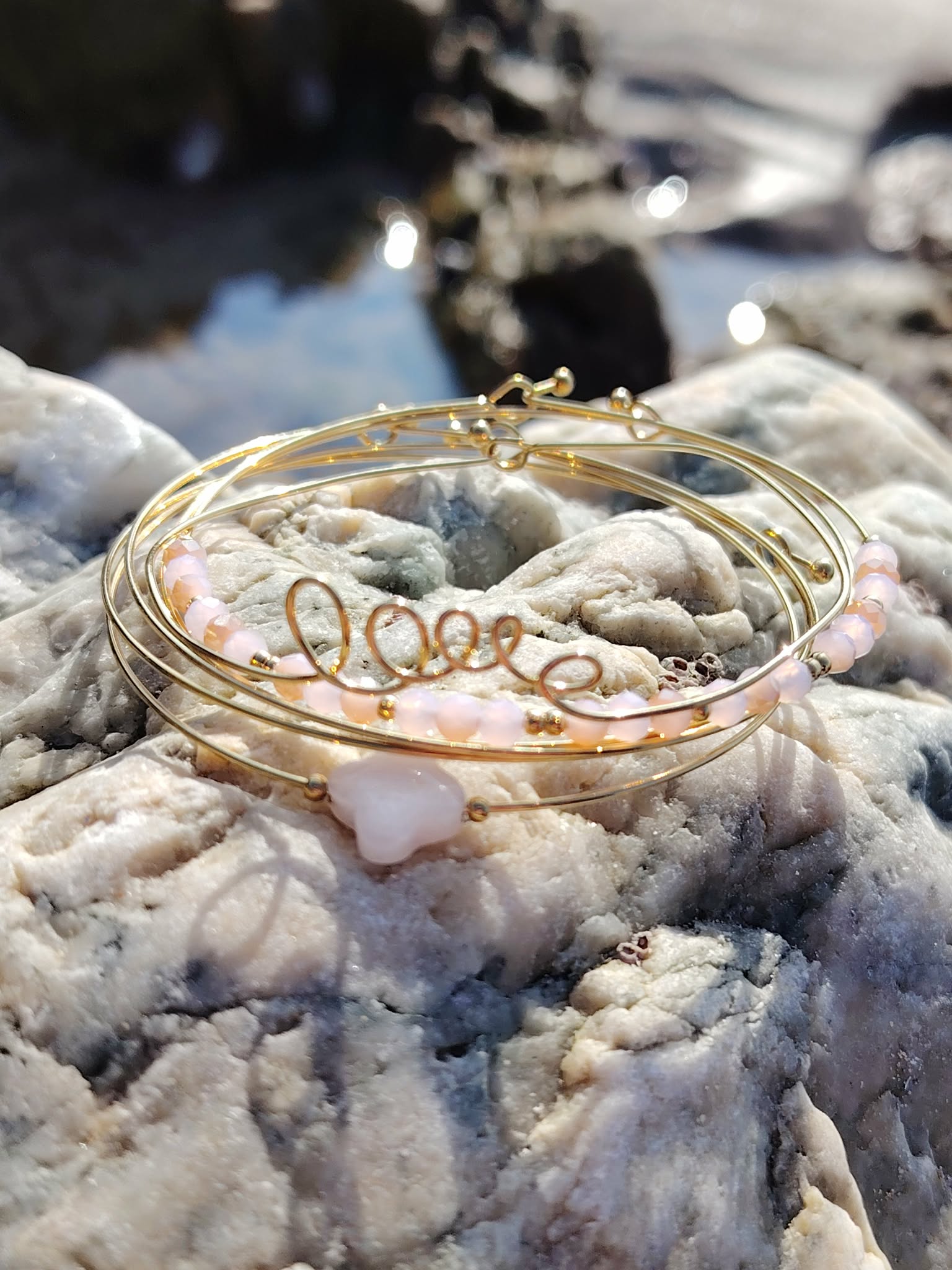 Bracelet semainier Love en quartz rose et acier inoxydable sur rochers en Bretagne près de l’eau, bijou romantique aux nuances rose poudré