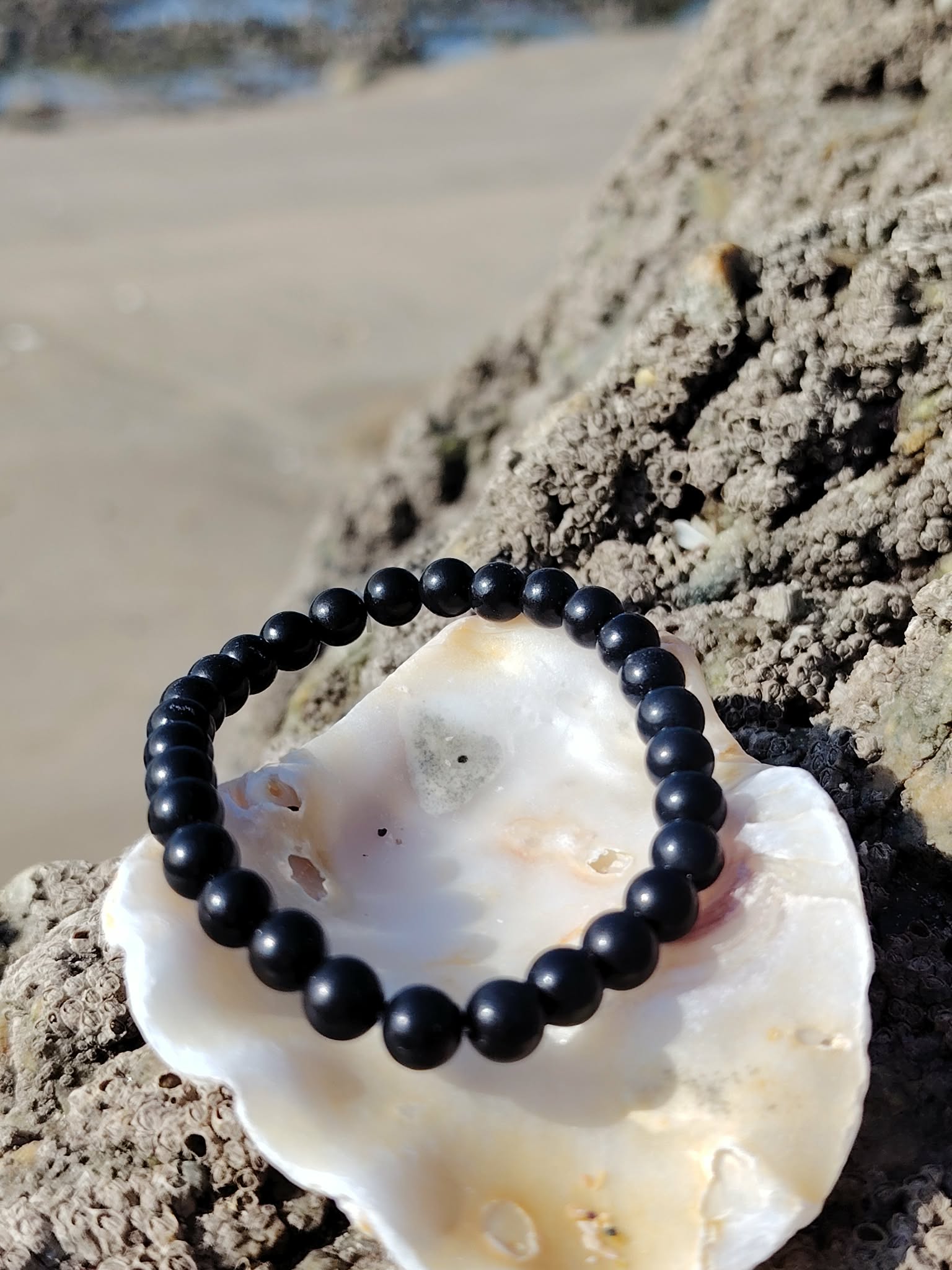 Bracelet shungite 6 mm sur coquillage blanc et bois flotté sculpté, lumière dorée en arrière-plan, relâchement profond et énergie plus posée