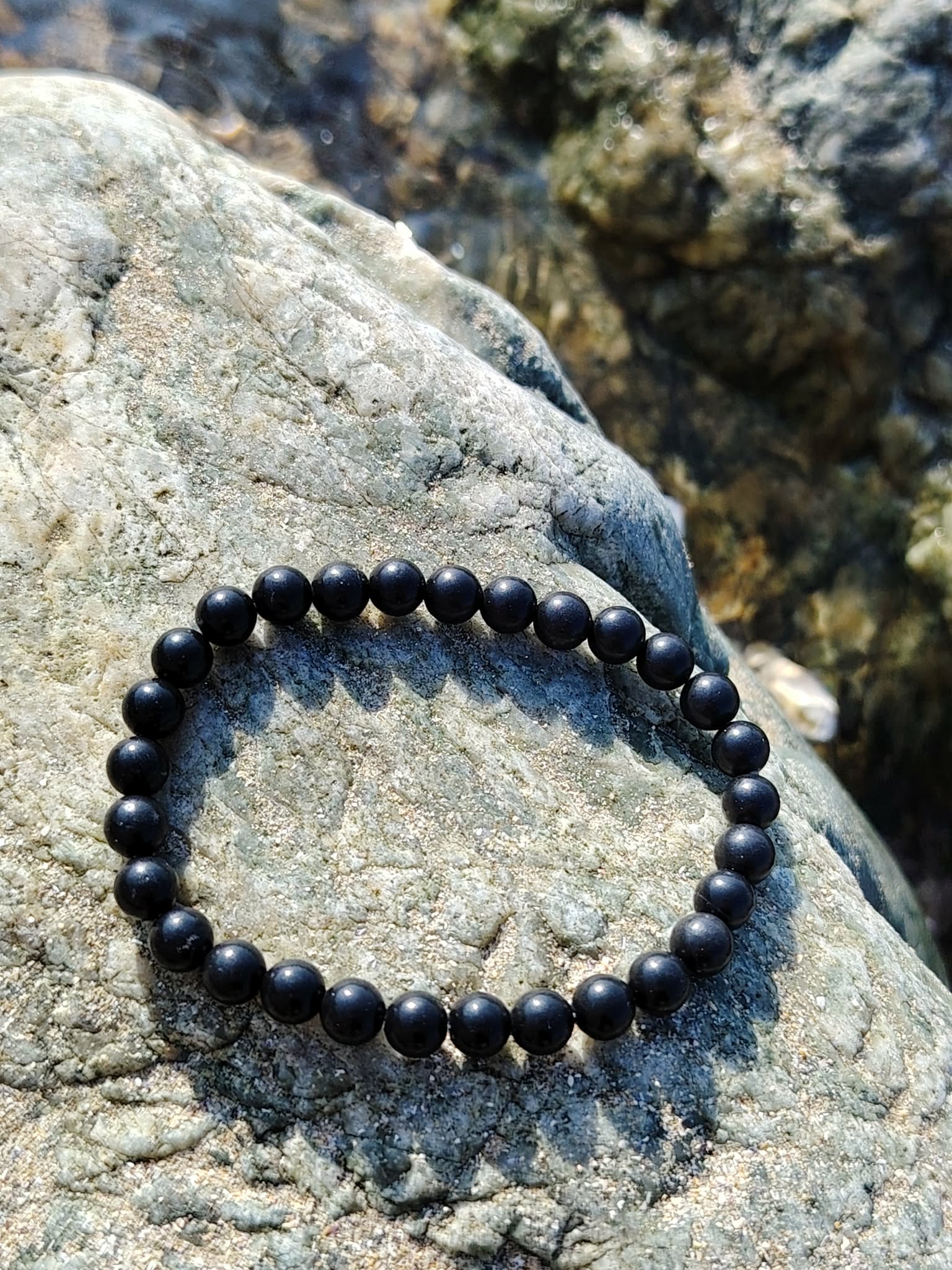 Bracelet shungite 6 mm sur galet clair au soleil, ambiance minérale en Bretagne, stabilité du ressenti et protection face aux tensions extérieures