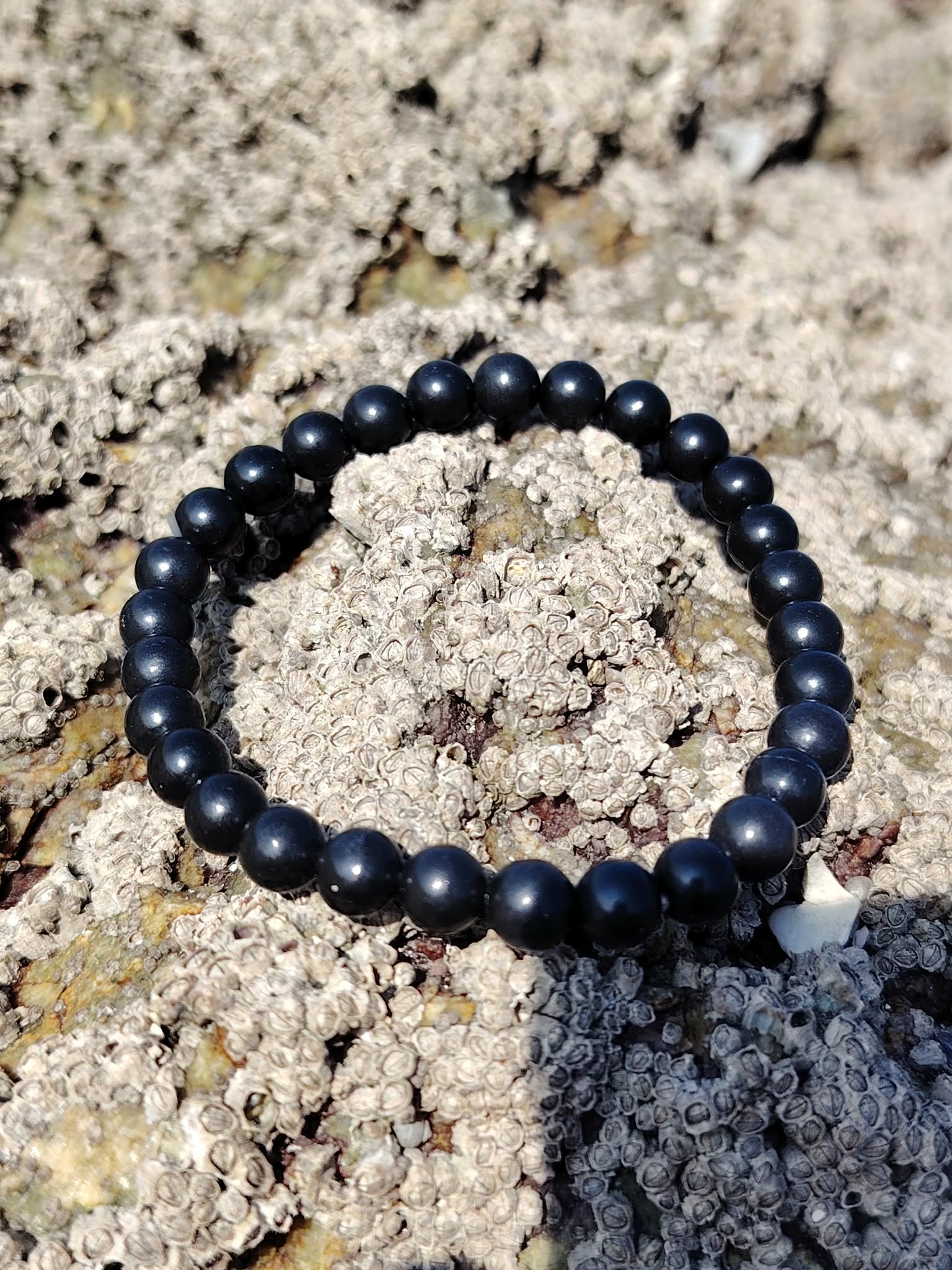Bracelet shungite 6 mm en cercle sur écorce beige veinée, photo Bretagne, recul mental, ancrage net et endurance émotionnelle