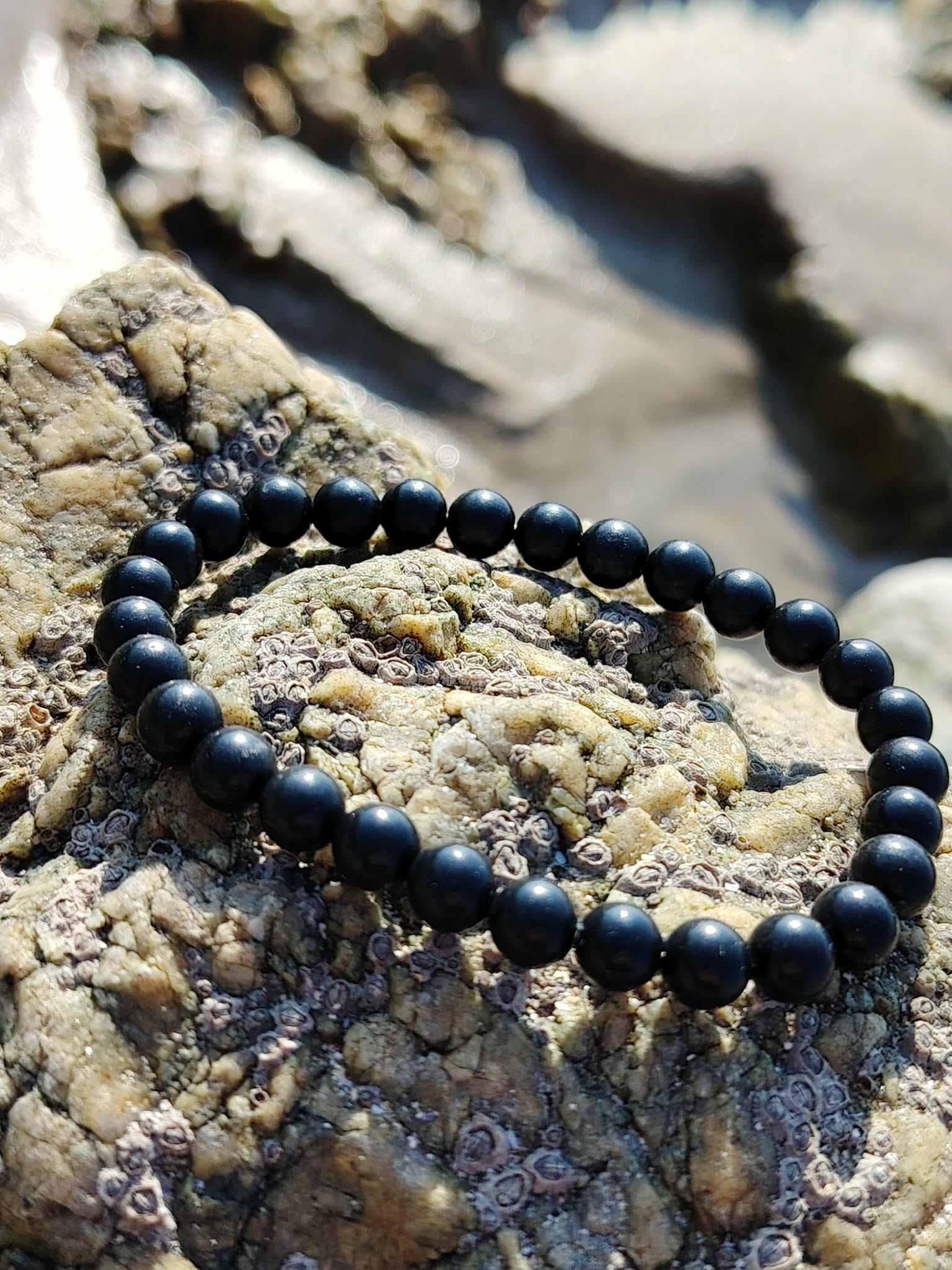 Bracelet shungite 6 mm noir intense en cercle sur roche claire et écorce sombre, présence ancrée, sobriété minérale et calme intérieur