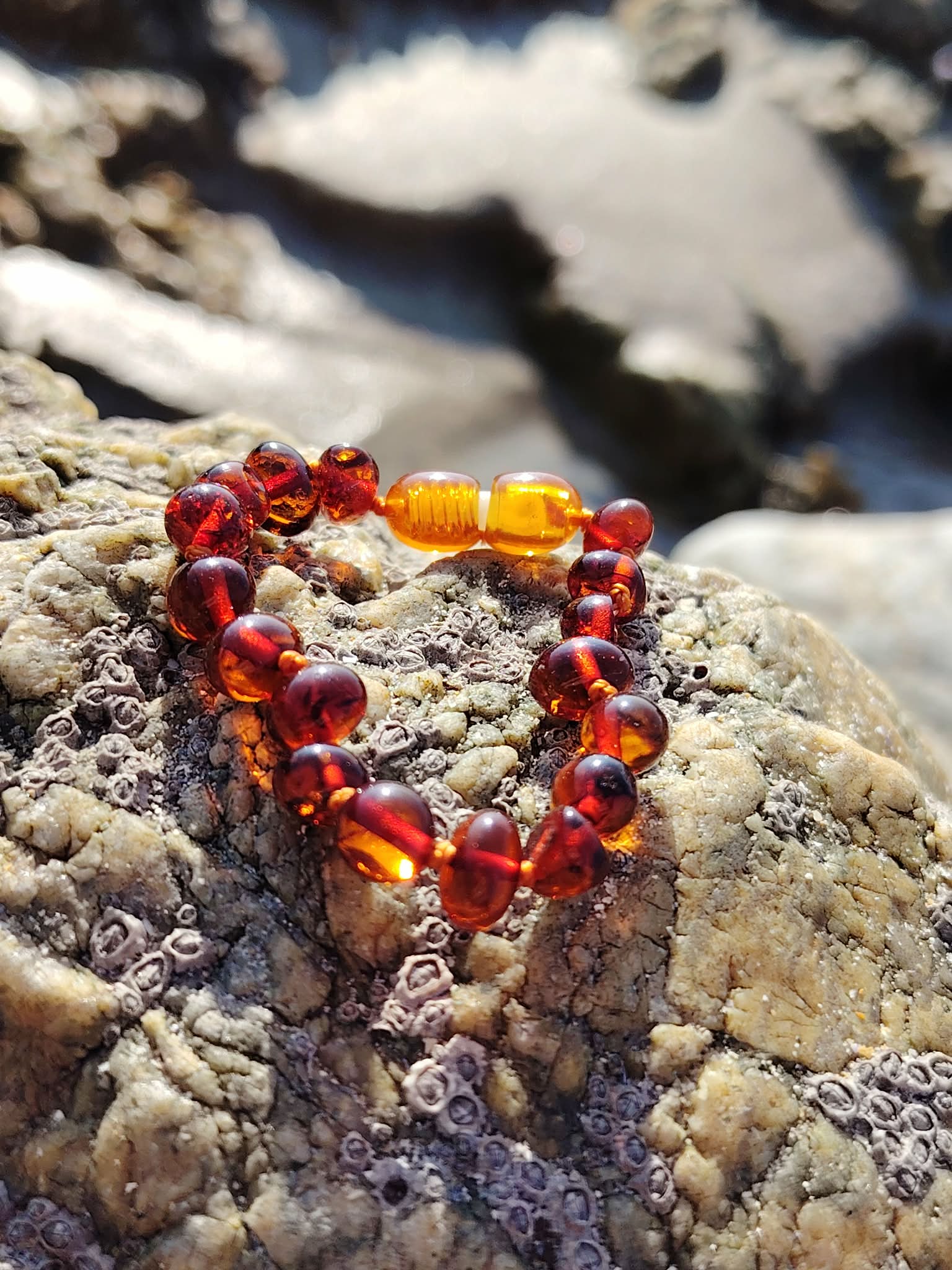 Bracelet bébé en ambre naturel sur rochers en Bretagne près de l’eau, perles miel cognac et fermoir de sécurité, bijou doux et lumineux