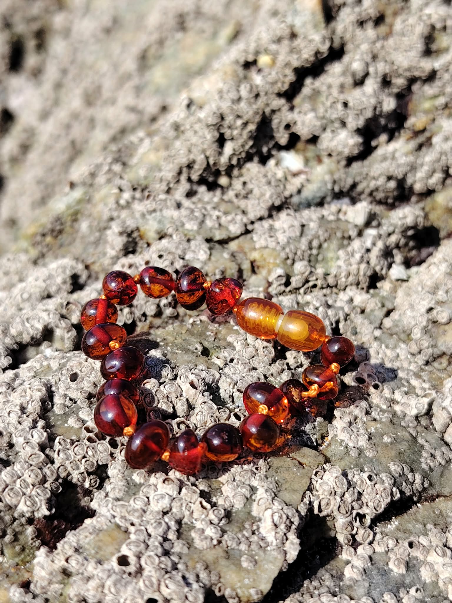 Bracelet bébé en ambre posé sur rochers bretons, bracelet enfant en ambre naturel aux tons chauds, photo nature au bord de mer