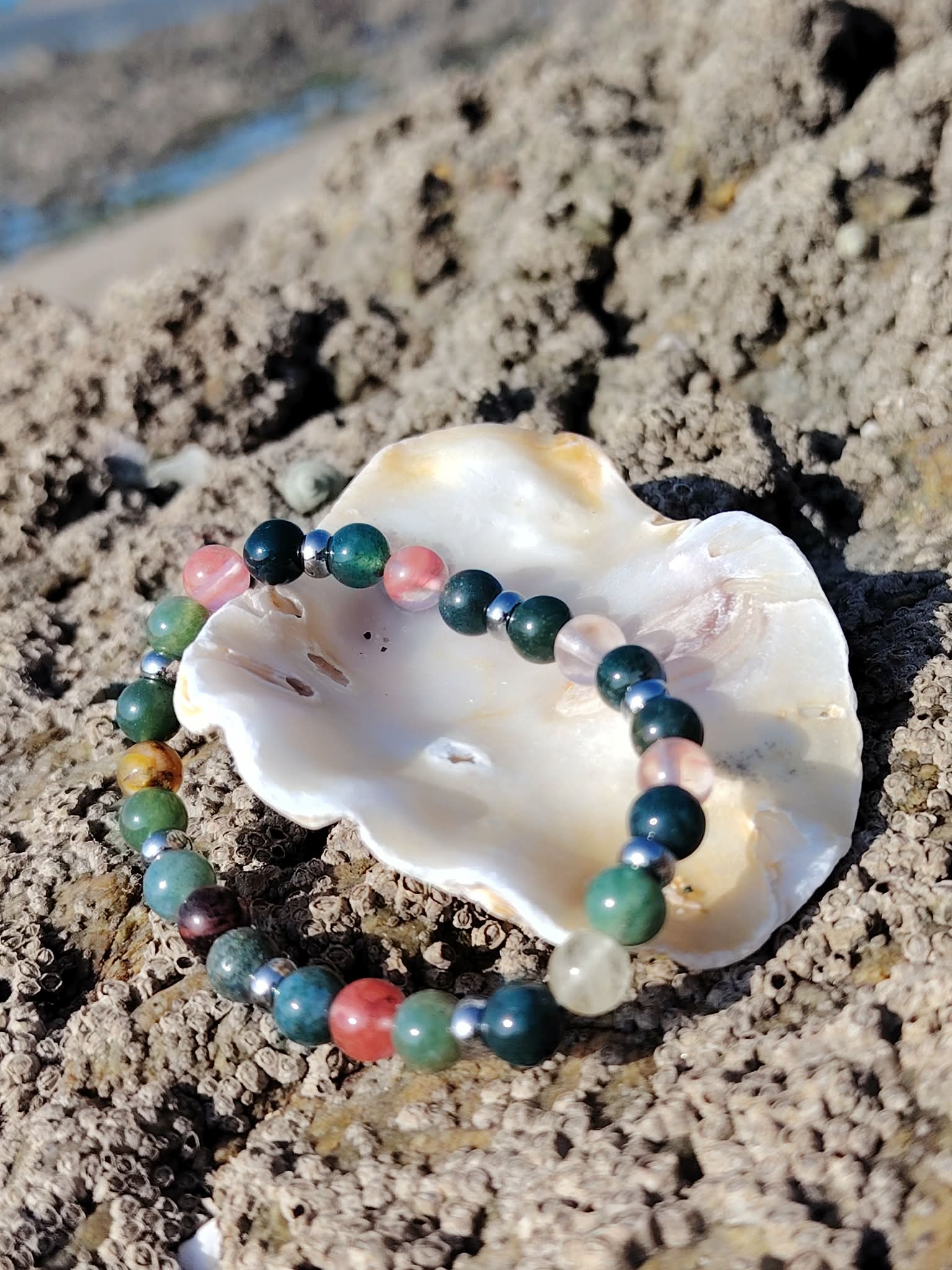 Bracelet chakra cœur en agate mousse et tourmaline melon d’eau présenté dans un coquillage sur rochers bretons, paix du cœur et relâchement émotionnel