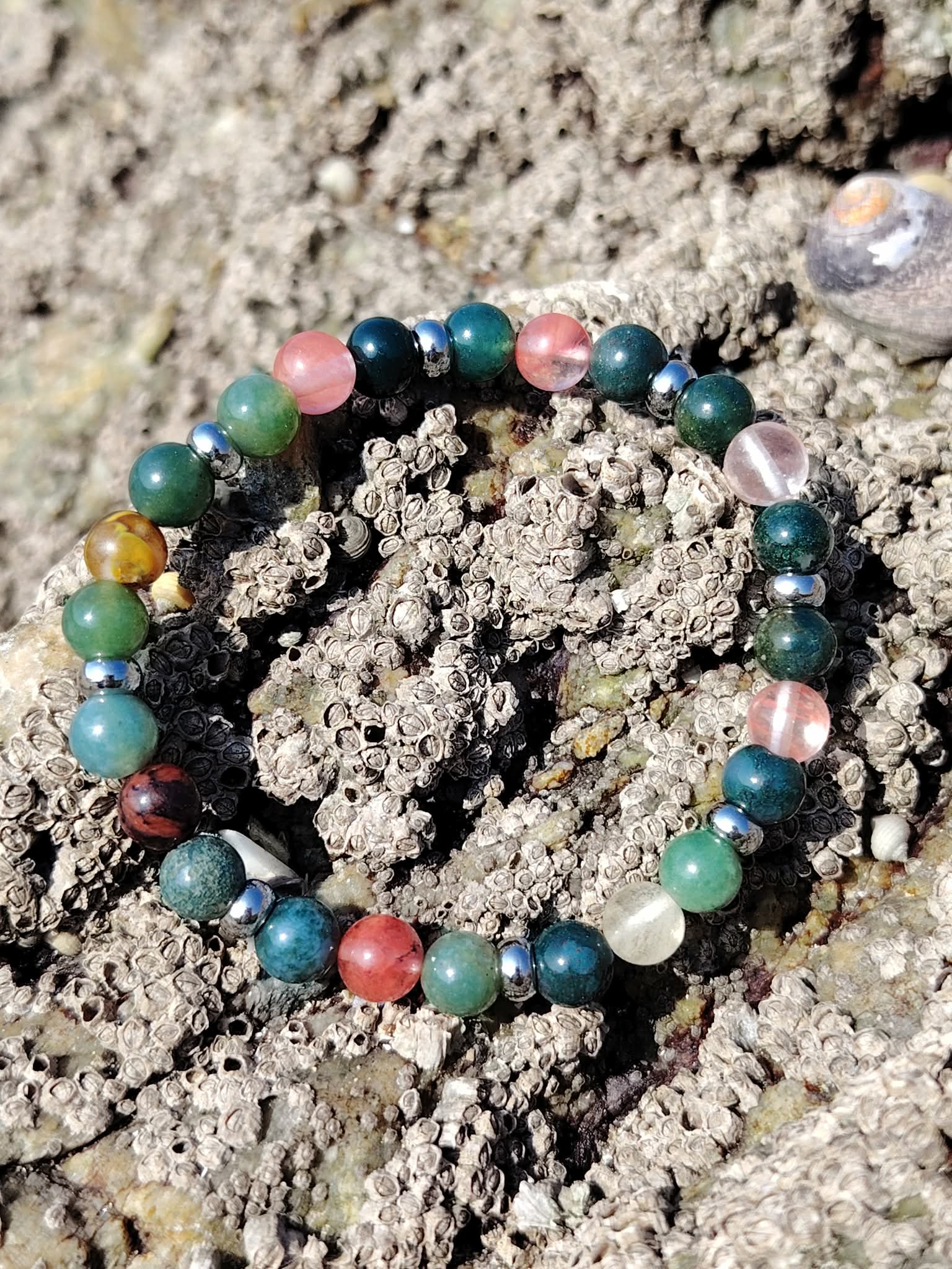 Bracelet chakra cœur photographié sur les rochers bretons, agate mousse et tourmaline melon d’eau pour ouverture émotionnelle, écoute de soi et harmonie intérieure