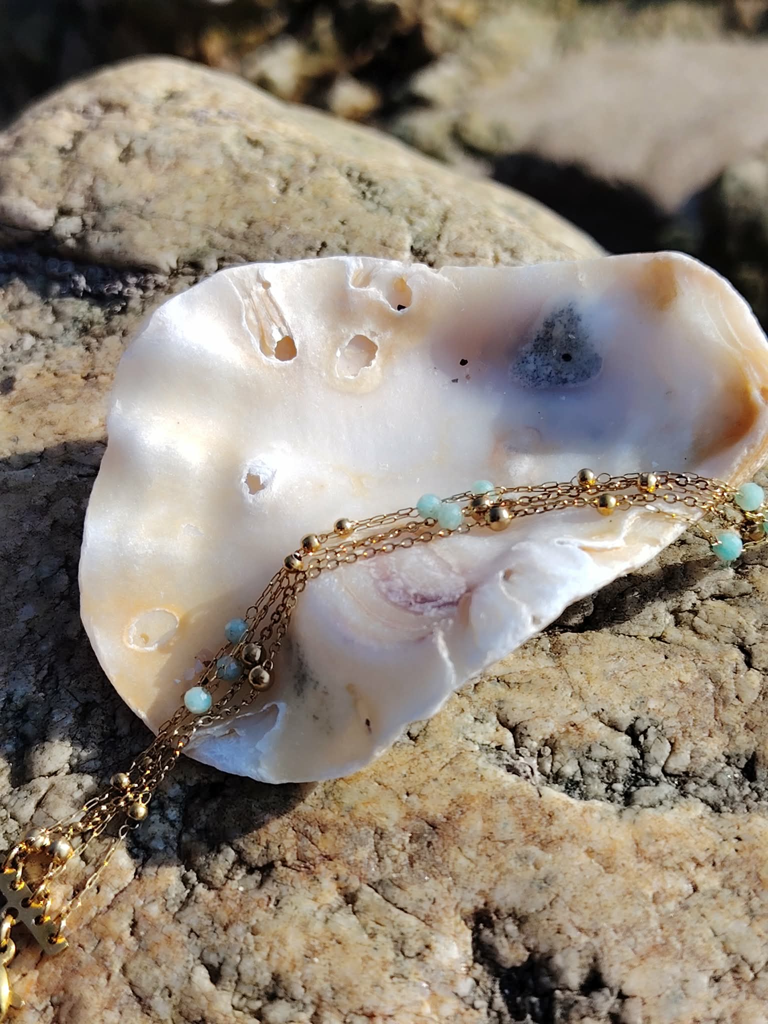 Bracelet amazonite facettée multi-rangs posé sur coquillage au milieu des rochers en Bretagne, perles bleu pastel et esprit bord de me