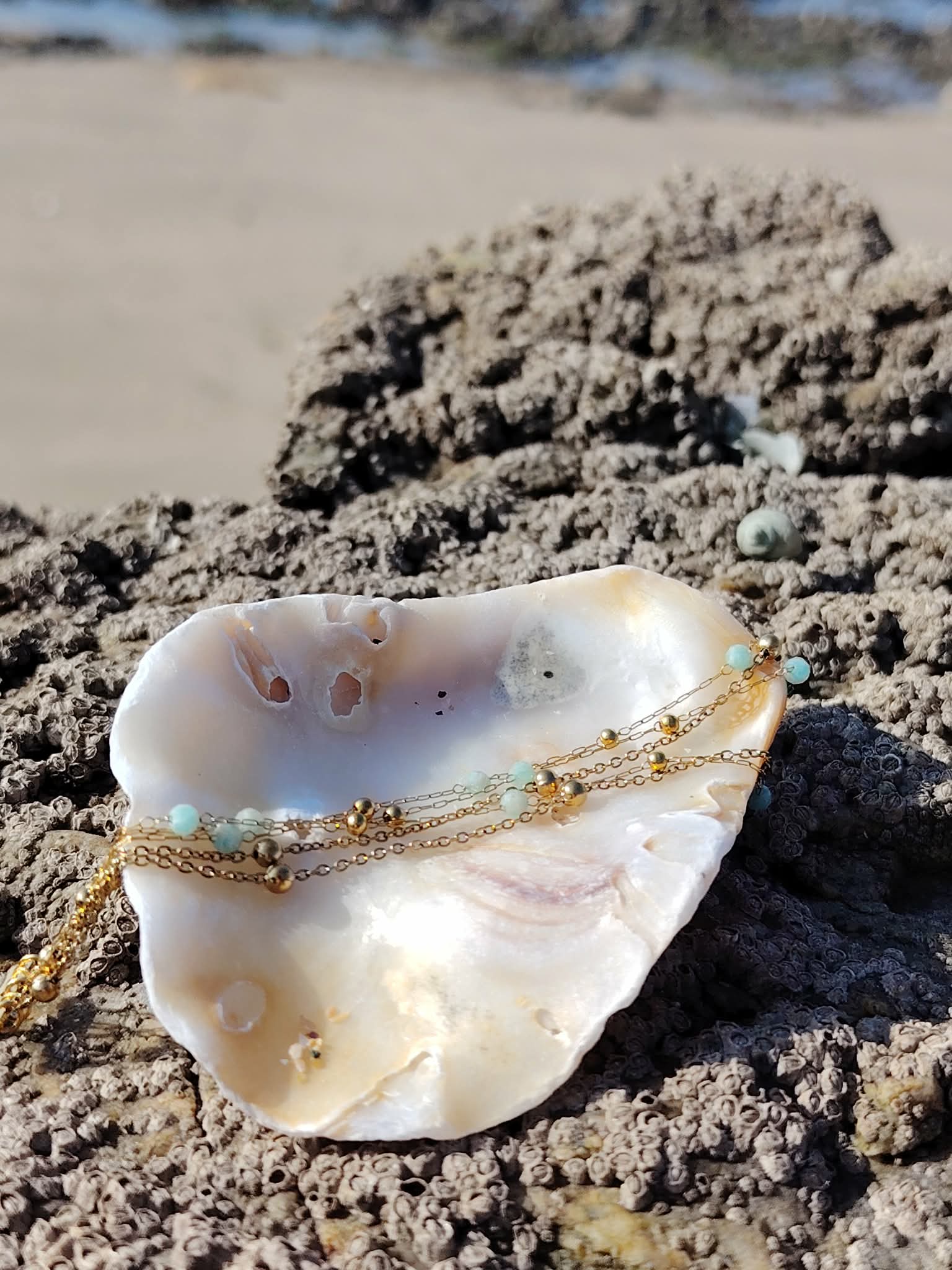 Bracelet doré multi-rang en amazonite facettée sur roche et coquillage en Bretagne, détail lumineux des chaînes et perles bleues