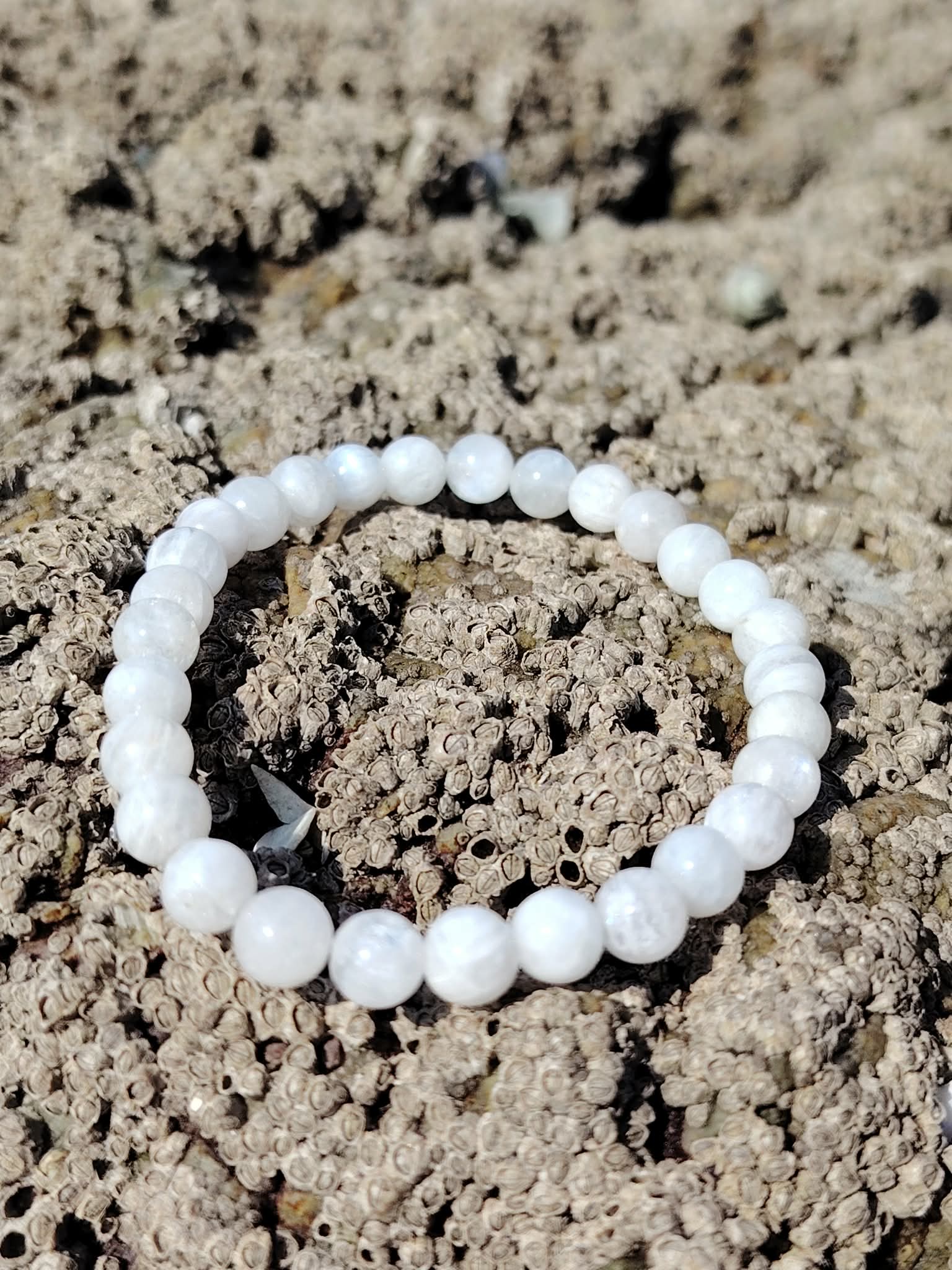 Bracelet pierre de lune 6 mm blanc nacré en perles rondes posé seul sur le sable, photo Bretagne, évoquant l’écoute intérieure, la sensibilité