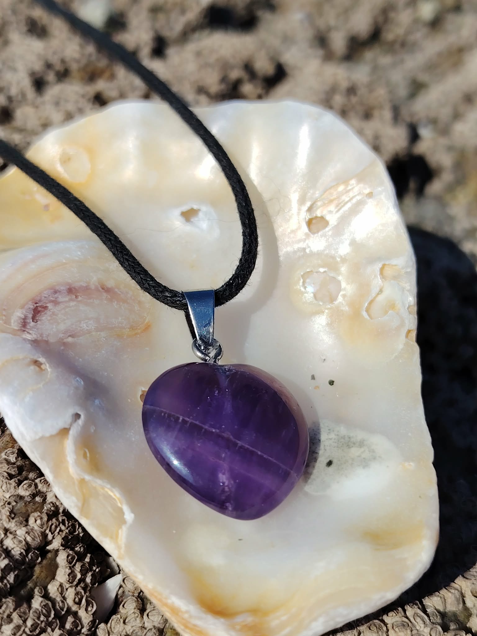 Pendentif cœur en améthyste sur cordon noir, présenté sur un coquillage en Bretagne, douceur intérieure, intuition calme et sérénité du cœur
