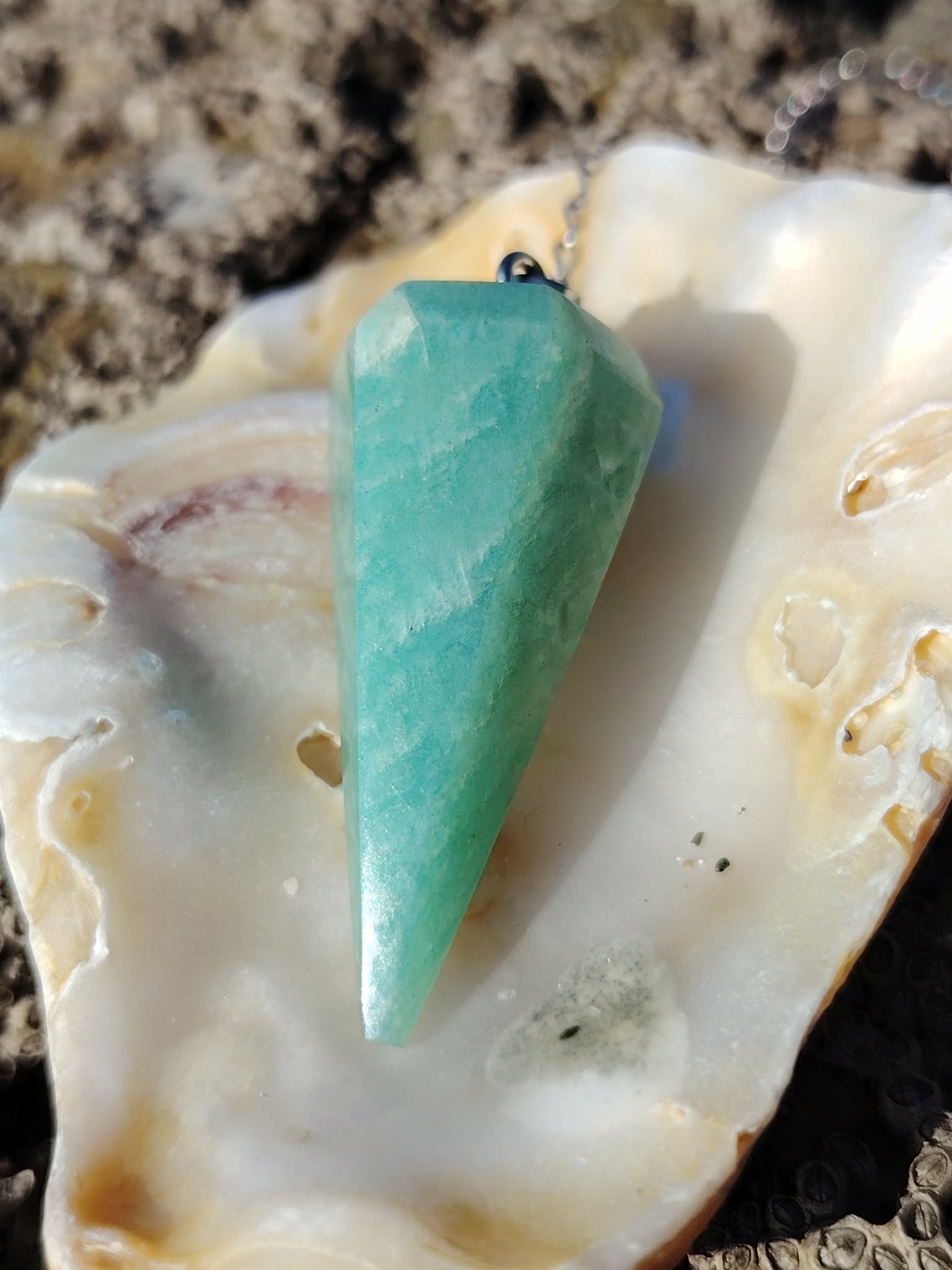 Pendule en amazonite bleu-vert dans un coquillage posé sur roche en Bretagne, photo douce évoquant apaisement, intuition et équilibre.