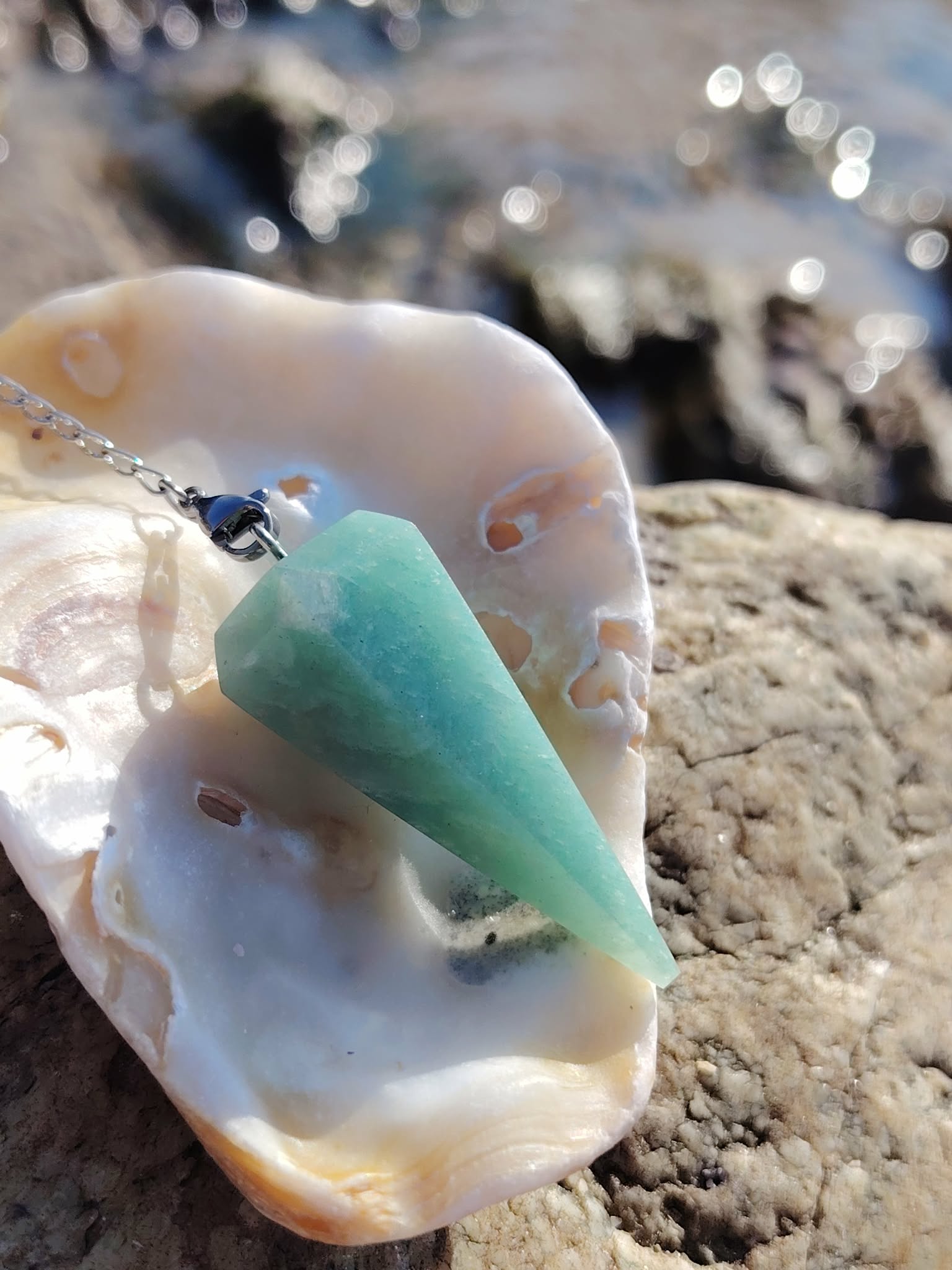 Pendule en amazonite bleu-vert dans un coquillage sur rocher en Bretagne, photo apaisante évoquant douceur, clarté et équilibre intérieur.